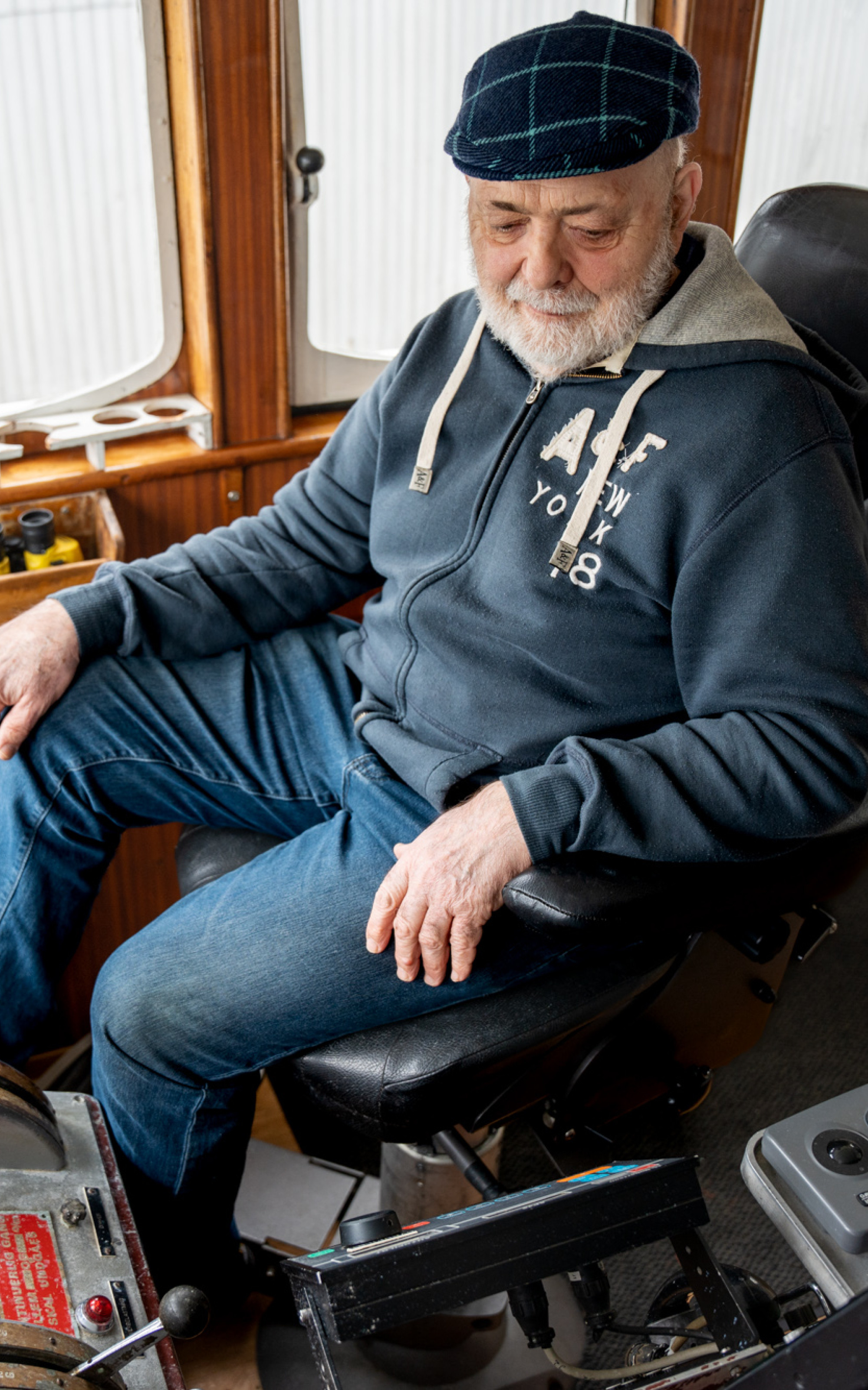 Eldre mann sit i pilotstolen på båten, med mykje instrument og spakar rundt seg.