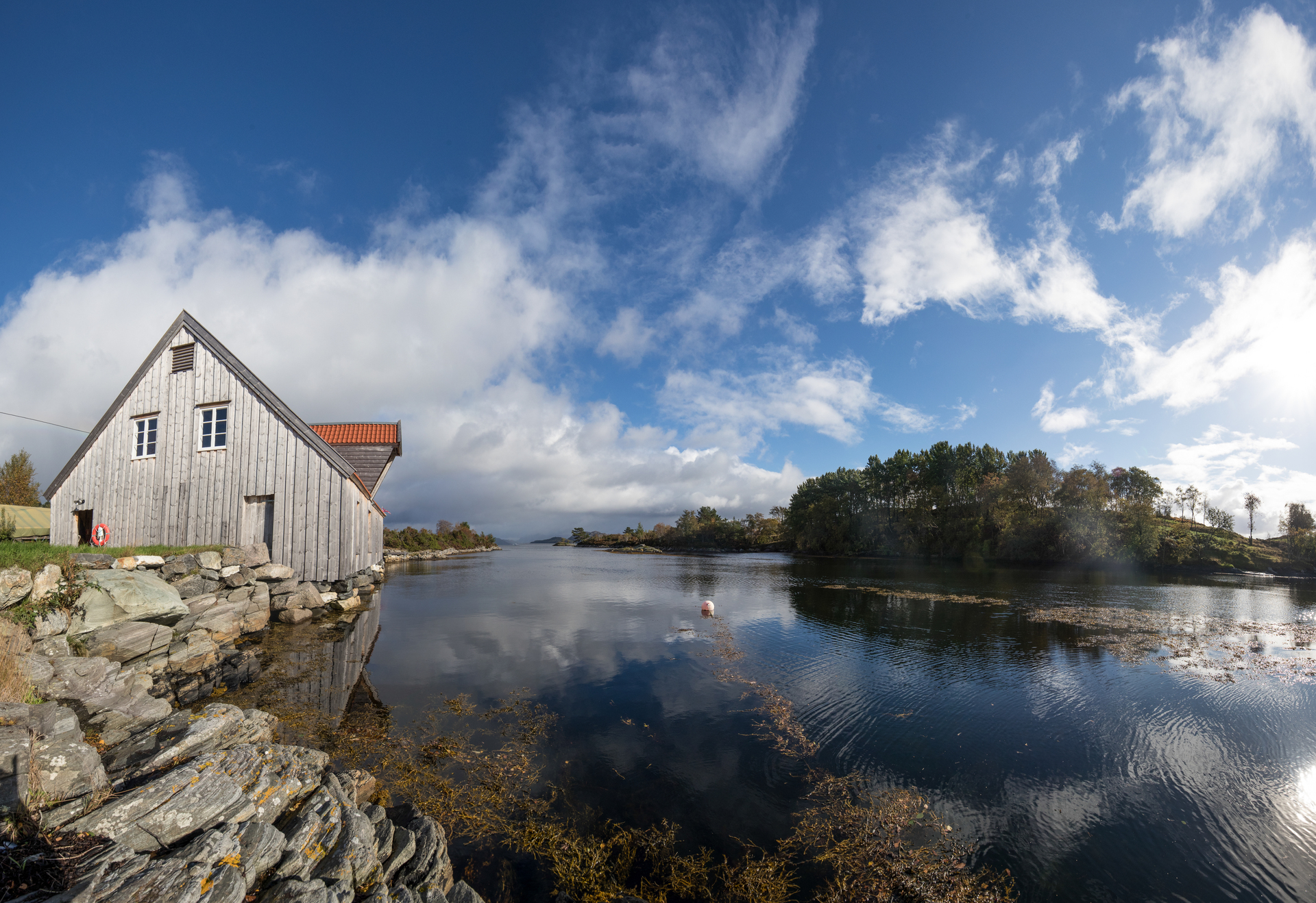 Oversiktsbilde over Bataldebua ved sjøen og Brendøya i bakgrunnen. Blå himmel og rolig sjø.