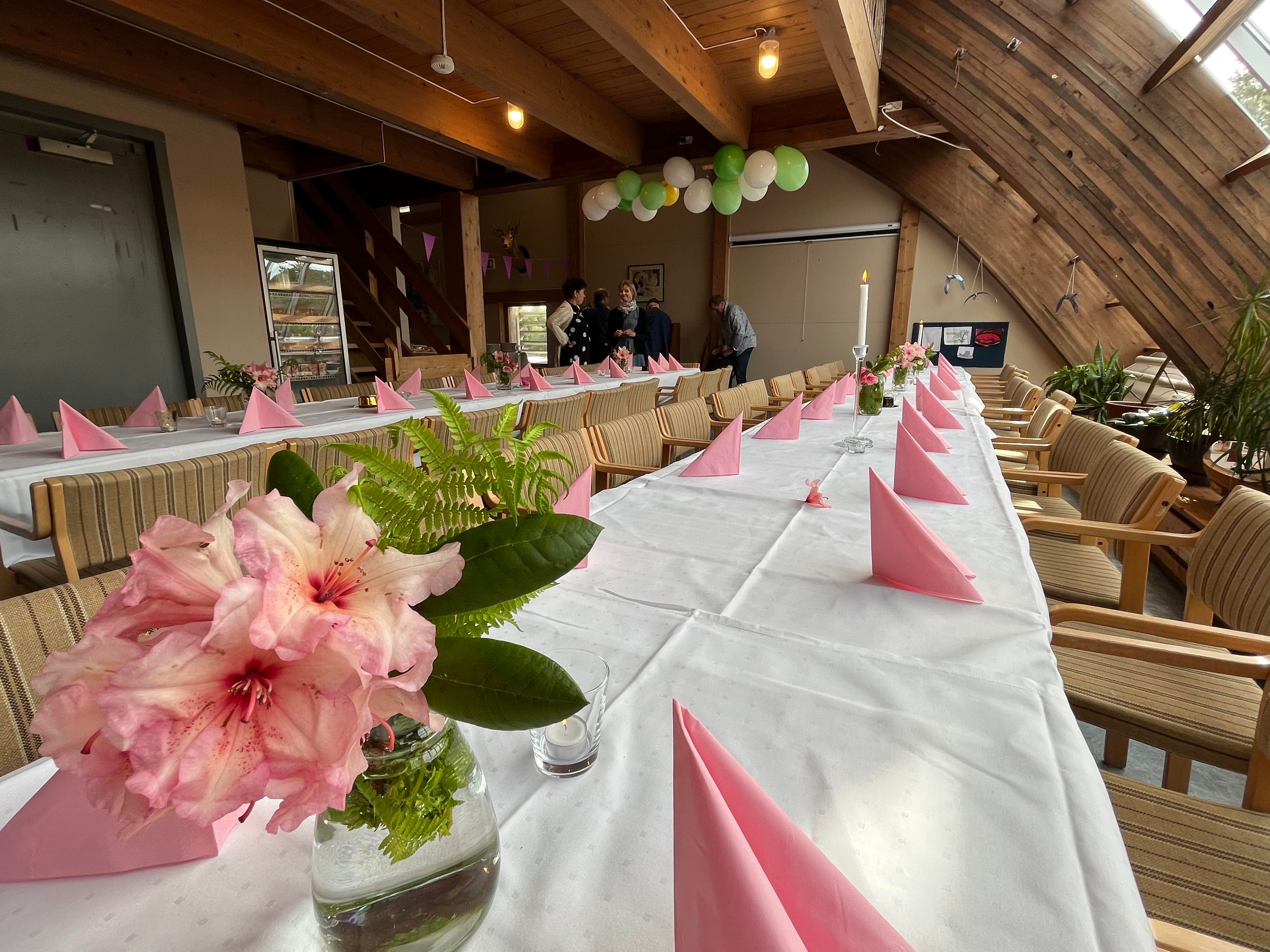 To langbord i kafeen på Kystmuseet er dekka med kvit duk, rosa seriviettar og blomar - ballongar i taket