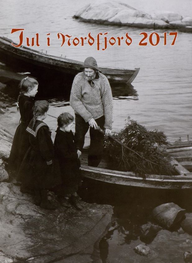 Framside av Jul i Nordfjord frå 2017. Mann i båt, har henta med eit juletre, nysgjerrige born ventar på land.