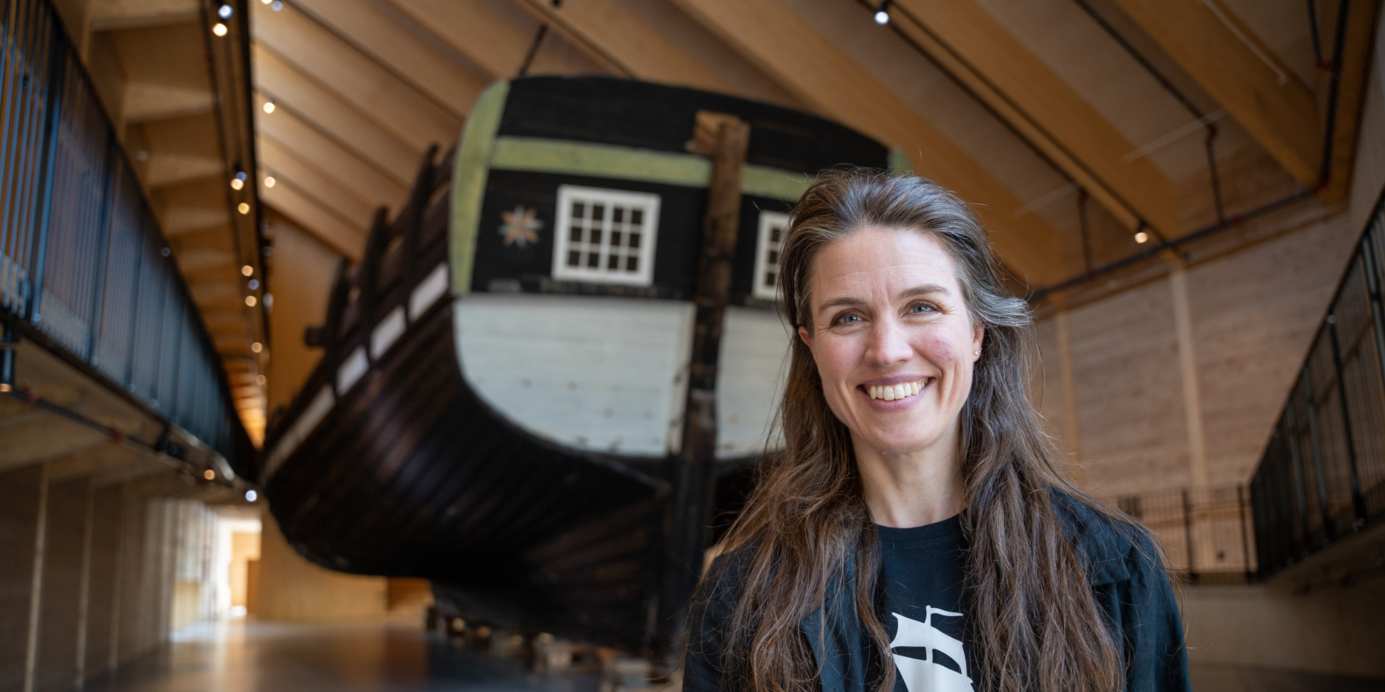 Portrait of smiling woman in front of boats stern inside museum.