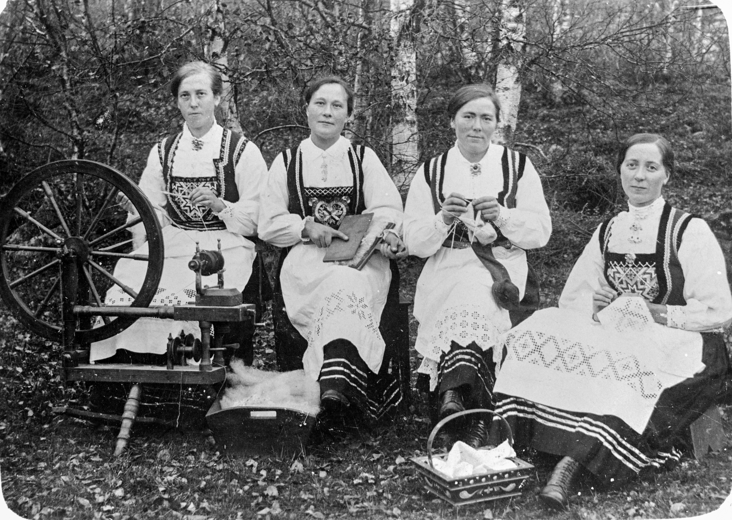 Kvinner i bunad som spinne ull på rokk, børstar ull med karder, strikkar og broderar.