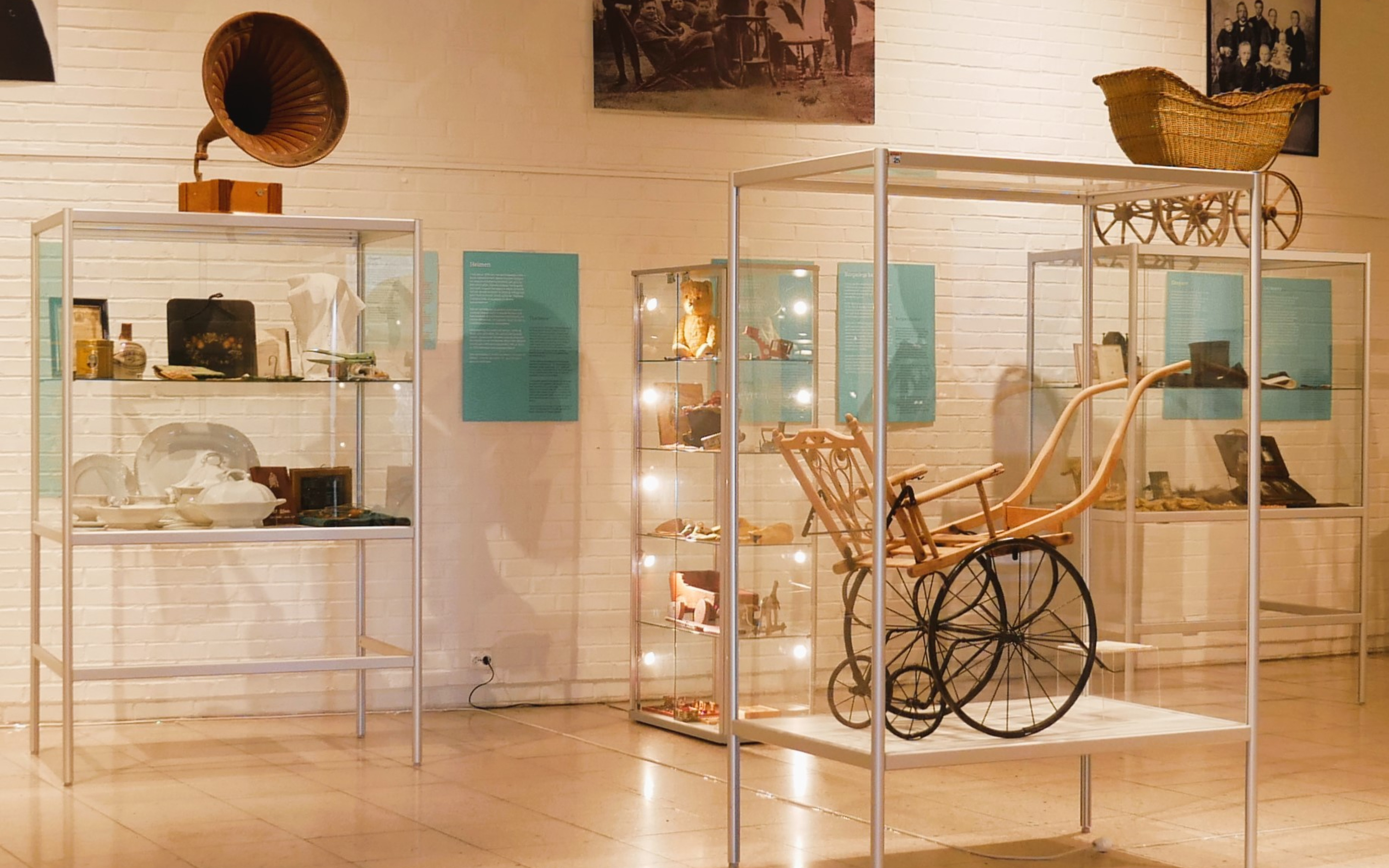 Et hvitt rom opplyst av lamper i taket. På utsiden av rommet er det grønne vegger, og en grønn plakat som står "Saman" på. Inne i rommet ser man monter i glass med gjenstander inni, blant annet en rullestol. På toppen av monterene står det en grammofon og en barnevogn. På veggene i bakgrunnen henger det grønne plakater, og fotografier av mennesker i sort-hvitt.