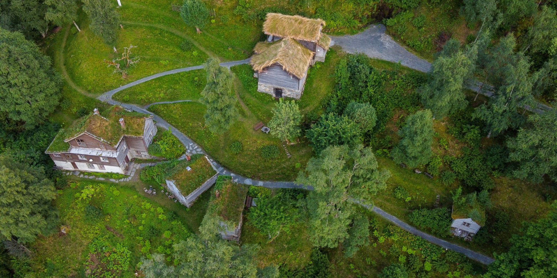 Flyfoto av kunstnharheimen til Nikolai Astrup, Astruptunet, der vi ser smale grusvegar bukte seg mellom grå bygningar med torvtak. Her kan du få omvisning.