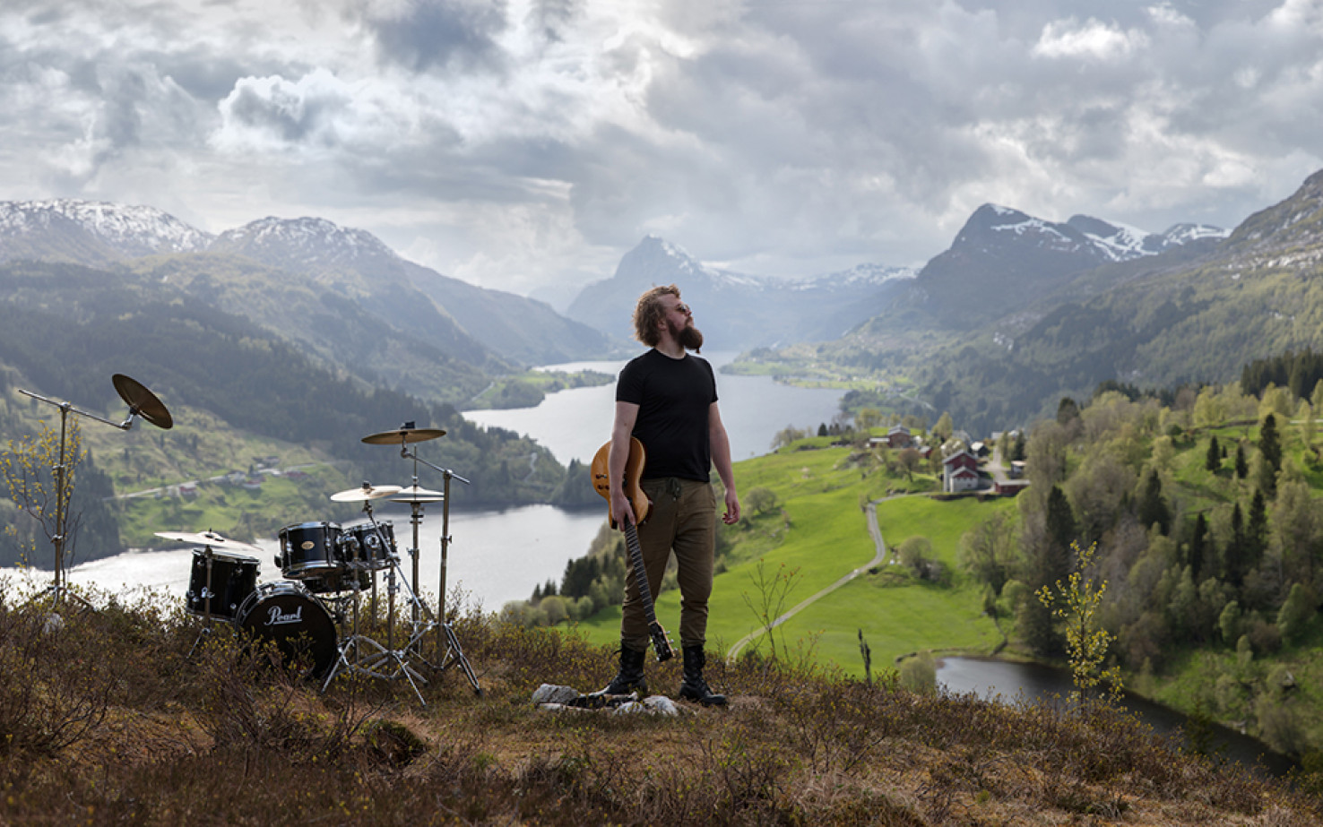Verksfoto av fotoverket Gaular av Oddleiv Apneseth. I midten av bildet står en mann, som ser opp mot høyre. I hånda hans har han en trehvit el-gitar. Til venstre i bildet, stående på bakken, er et trommesett. Bakgrunnen er storslått, med fjord og fjell. Himmelen viser stormskyer som kommer innover, men det er lysglimt ned i dalen.