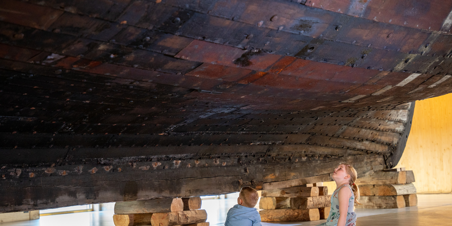 A boy and a girl sits under the hull og the Holvik Jekt.