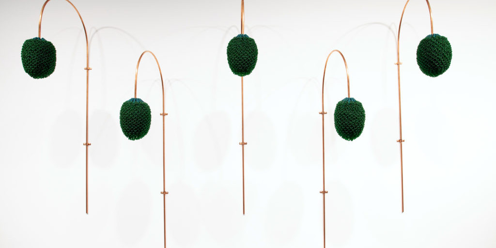 Utstilling viser bøgde koparrør med grøne, tekstilbaserte kongleaktive gjenstandar.