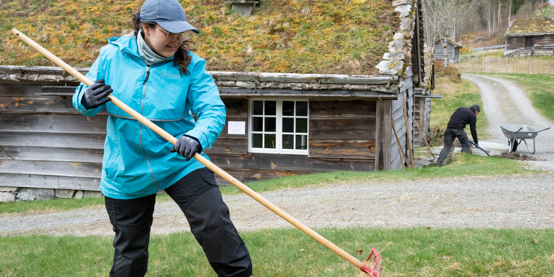 A woman rakes a yard at the museum.