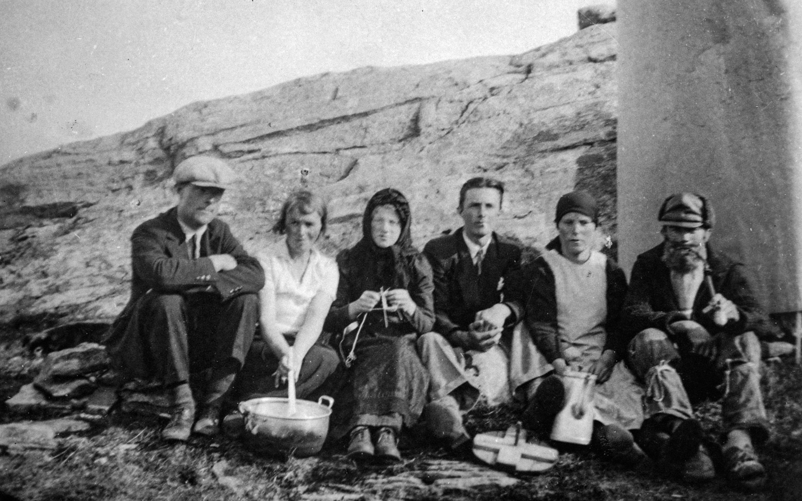 Gamalt svart/kvitt foto. 6 personar på fjell. frå venstre mann med mørk dress og lys luve, kvinne med kvit skjorte og mørkst skjørt. Kvinne med svart overdel og underdel og skaut. Mann med svart jakke, slios og lyse bukser. Kvinne med kvit kjole, mørk skjorte og mørkt skaut. Mann med skjegg og mørk luve, mørk jakke og bukse og kvit skjorte
