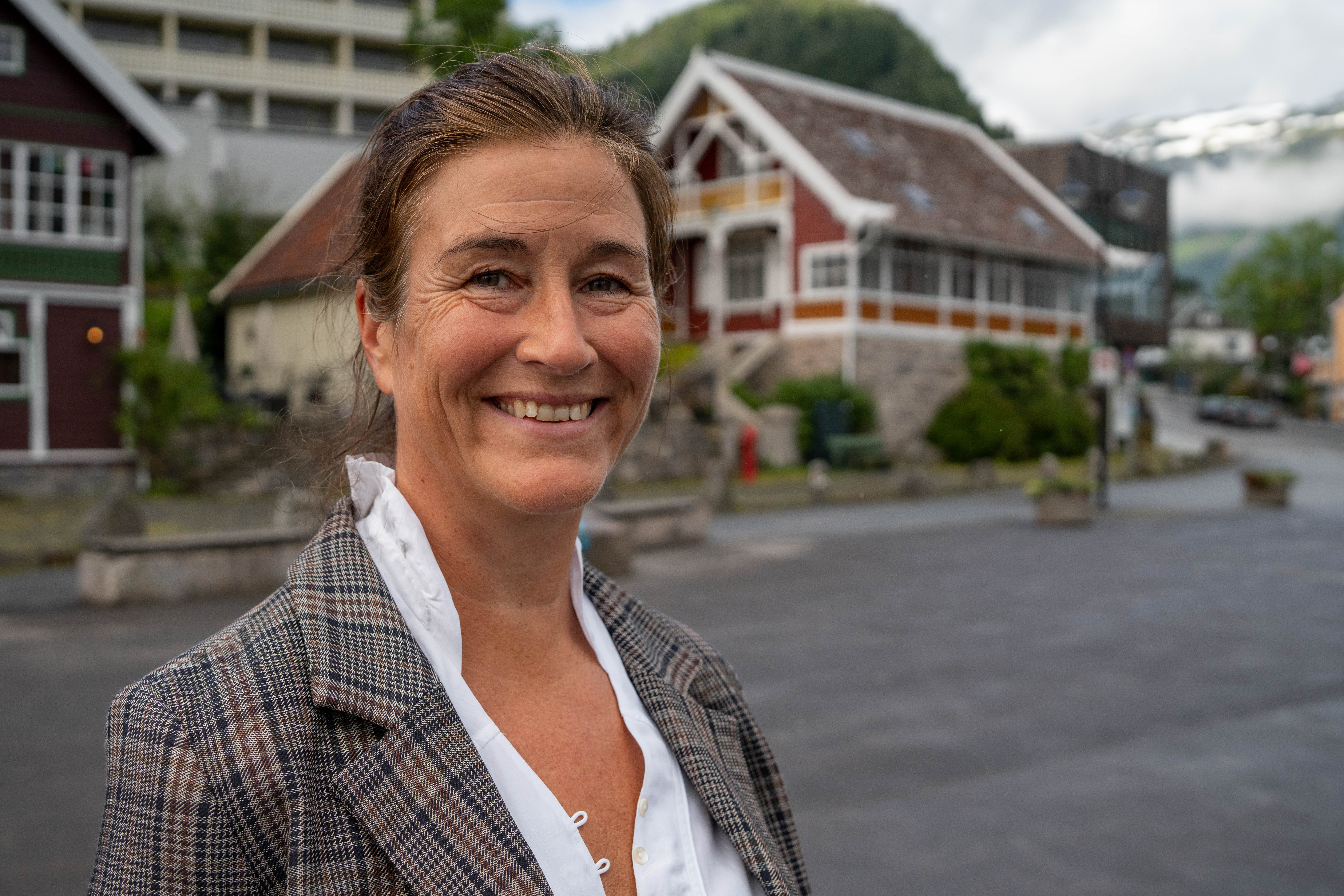 Guri Våge Mossige står framfor ei rekke med bygningar, inklusive Reiselivsmuseet.