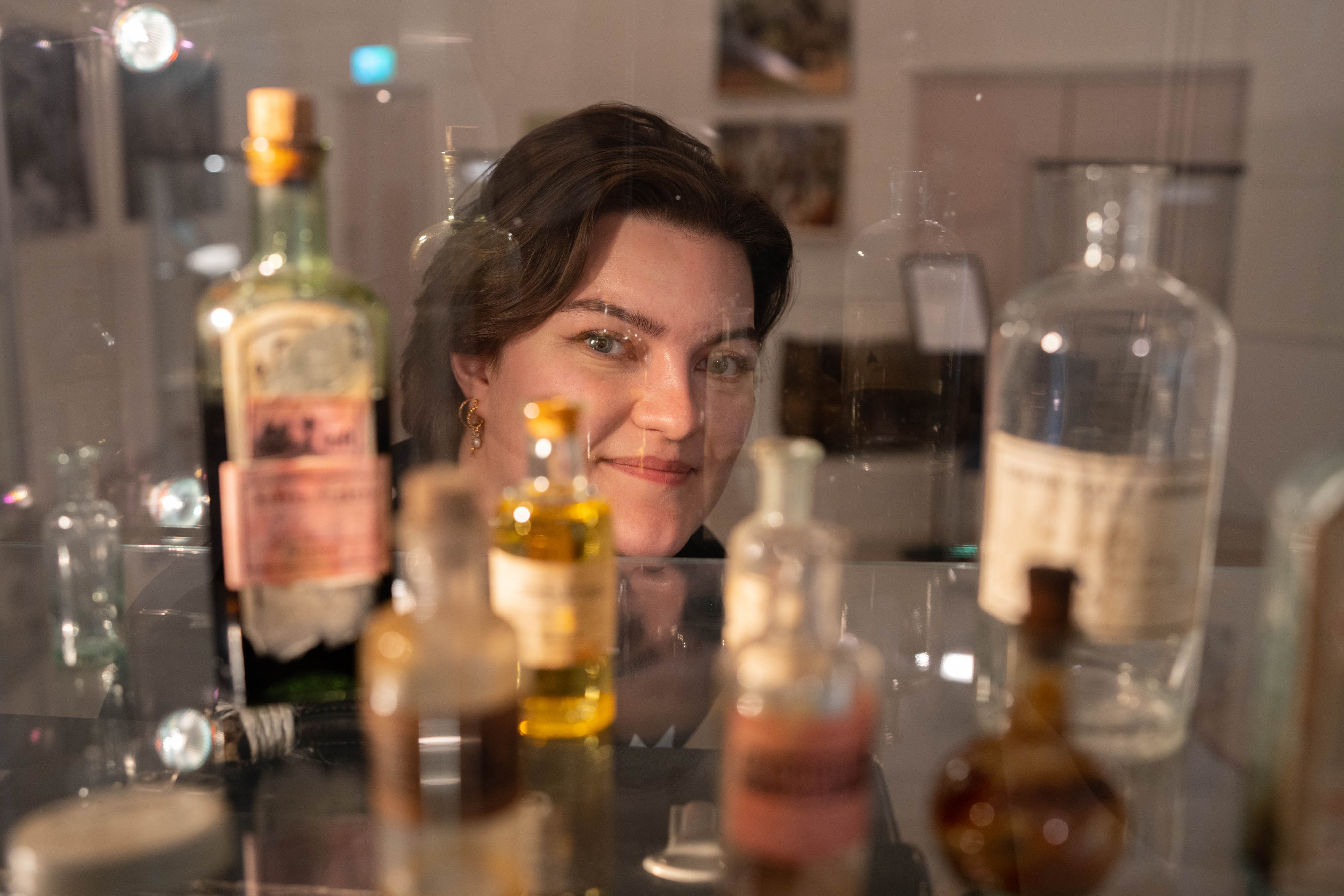 Museumspedagogen står bak ein gjennomsiktig monter med mange små, rare medisinflasker.