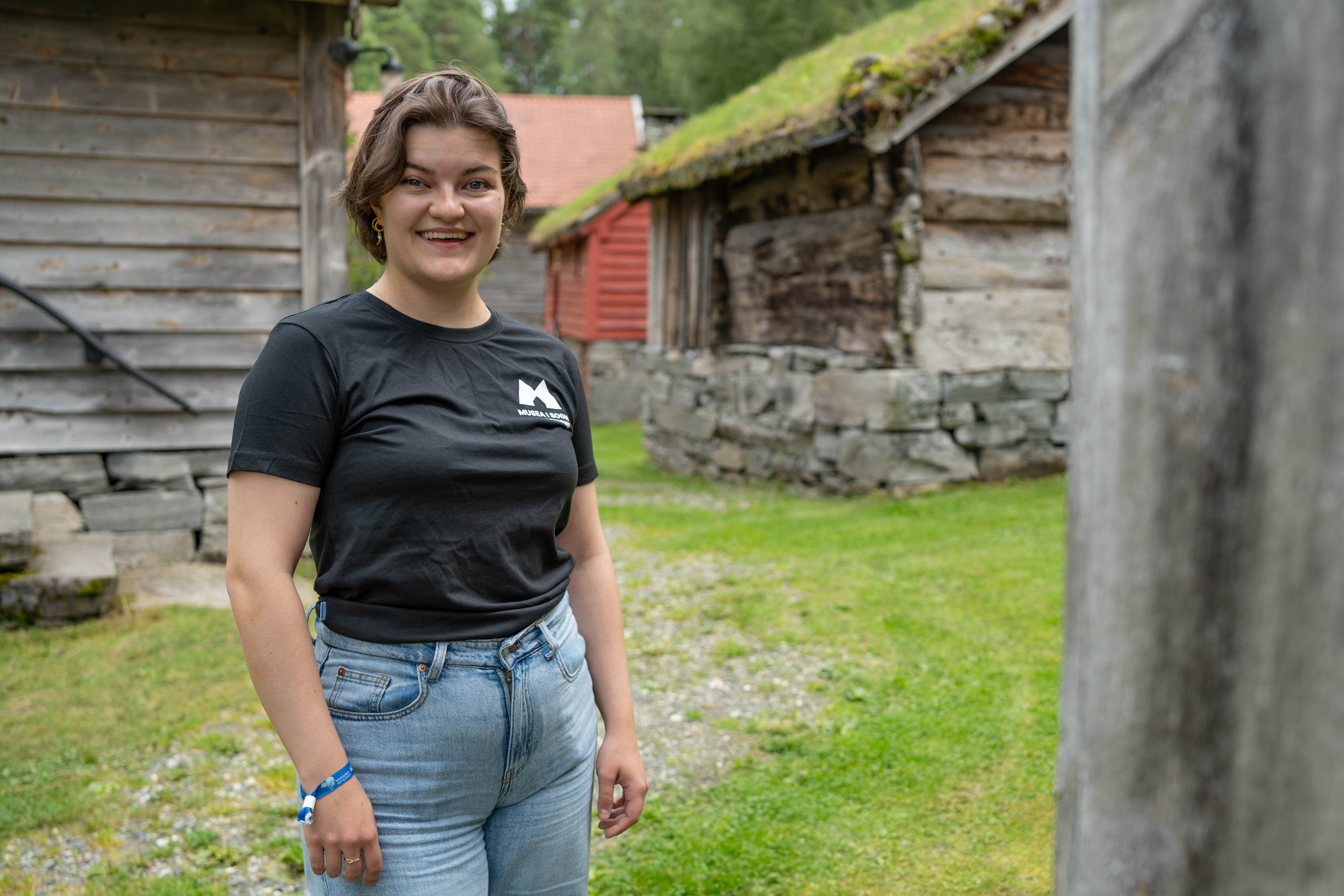 Museumspedagogen står framfor gamle, lafta hus.