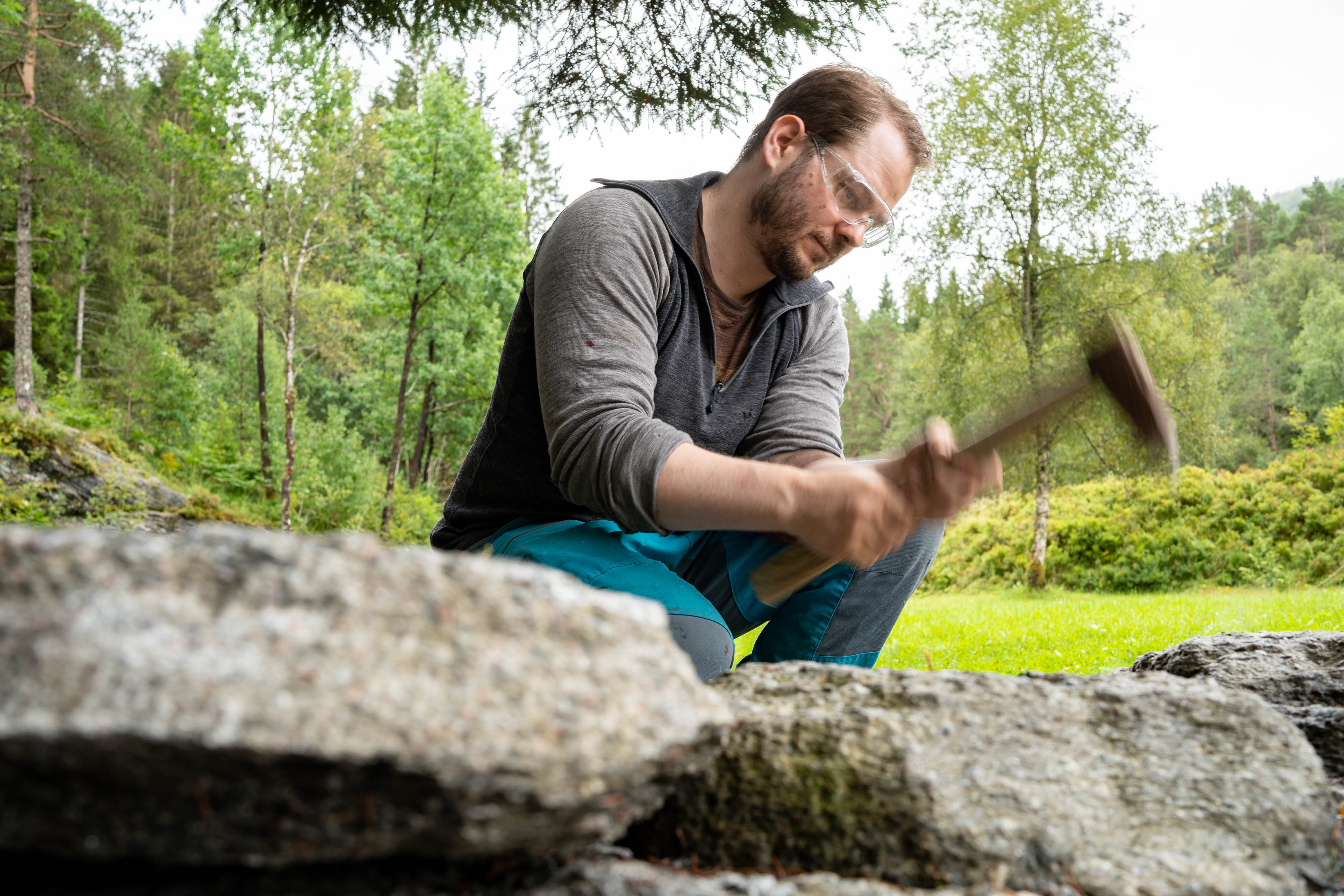 Ein tilsett med vernebriller hakkar ut ein kvernstein med tradisjonell hakke.