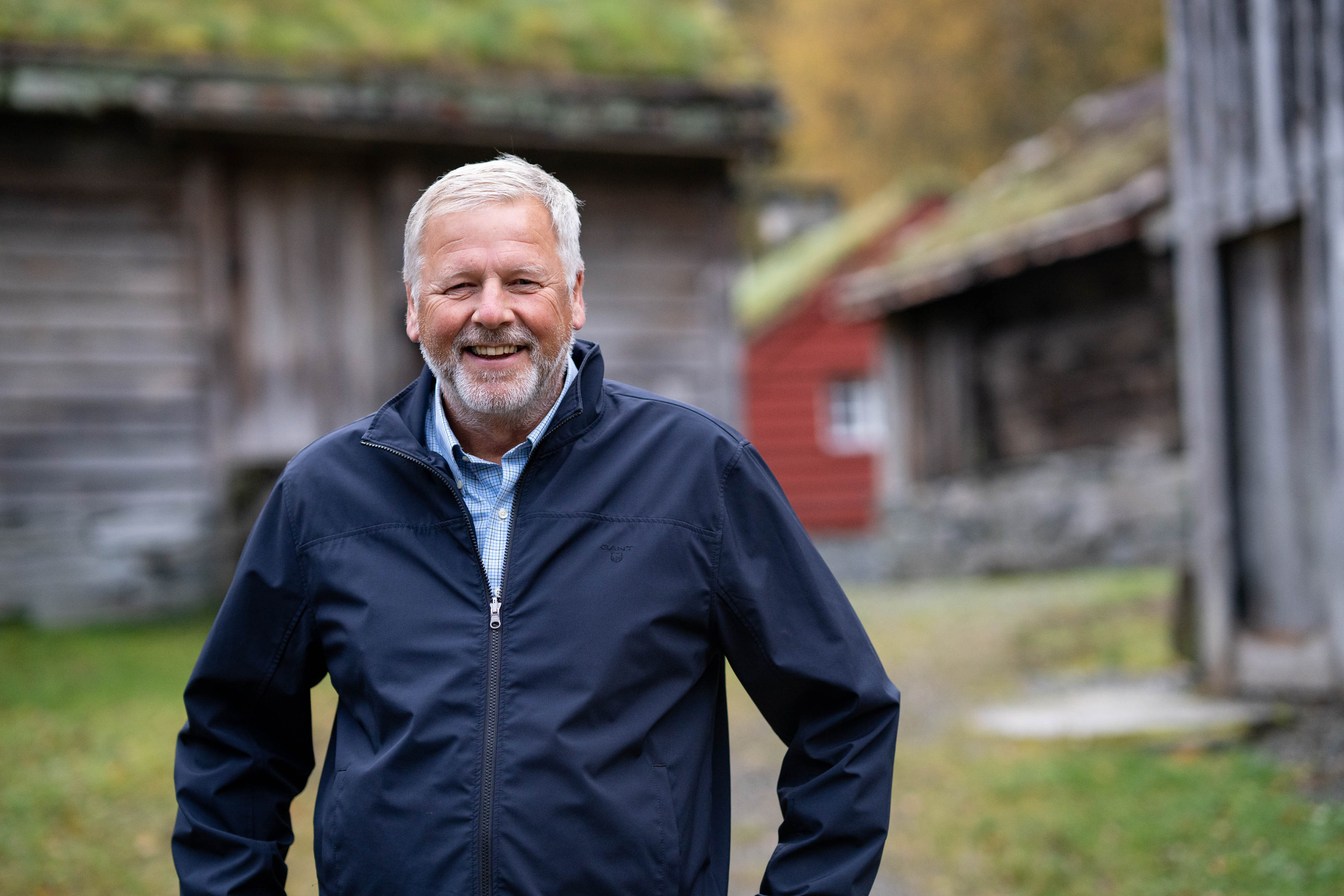 Jan Heggheim står og smiler framfor gamle museumsbygningar som er ute av fokus.