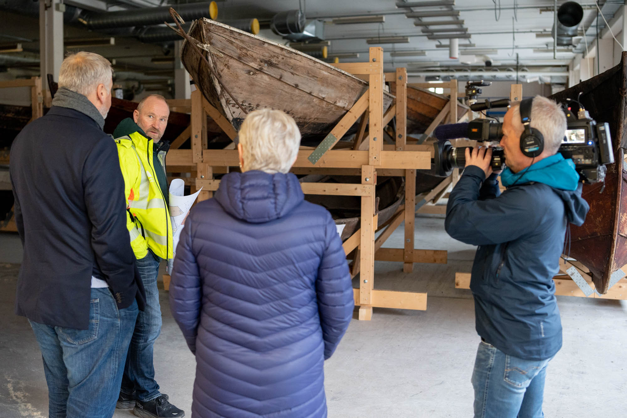 Omvising i båtmagasinet, der gamle trebåtar er stabla i stativ, to i høgda.