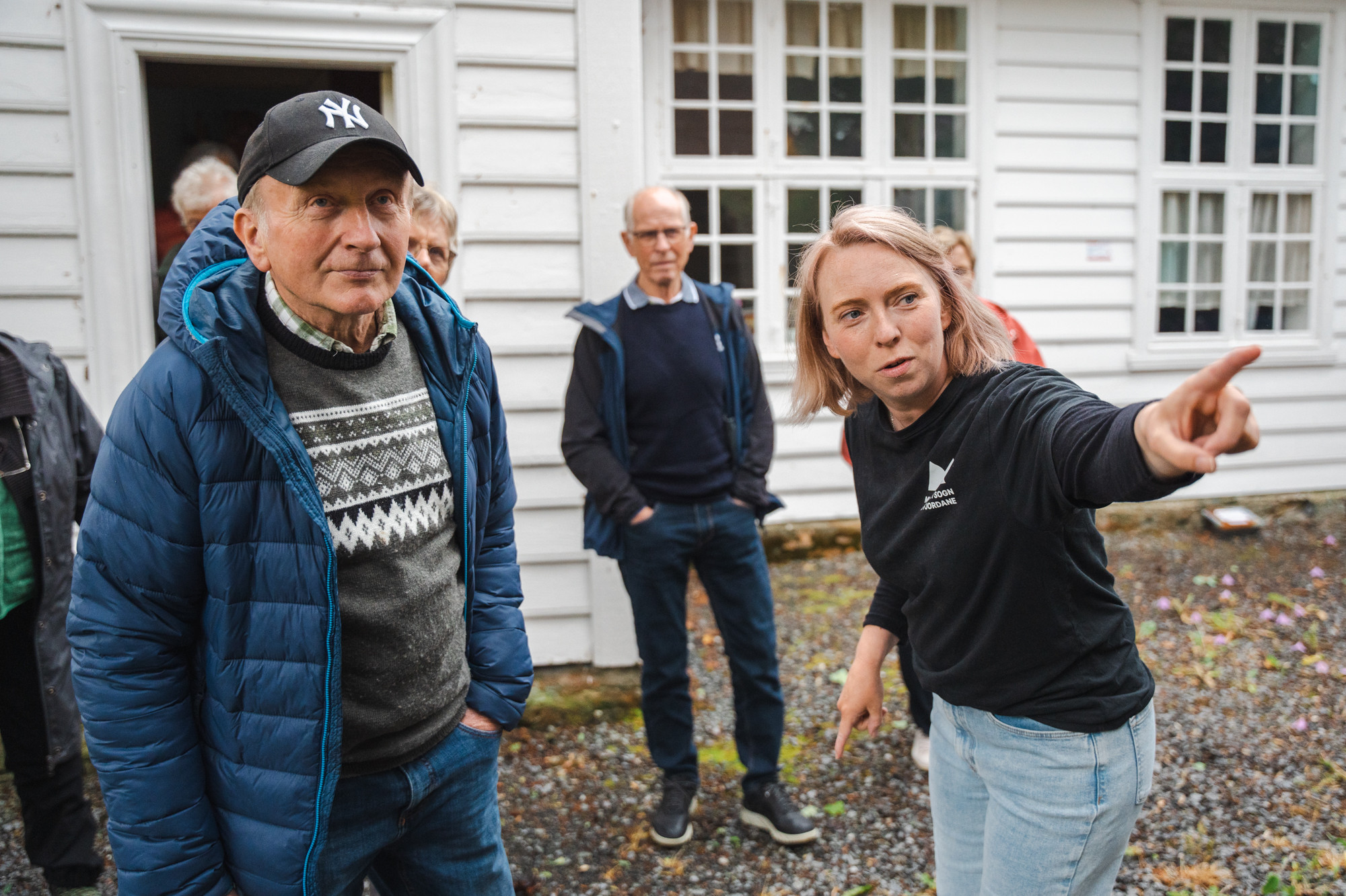 Engasjert kvinne peikar, eldre menn ser på.