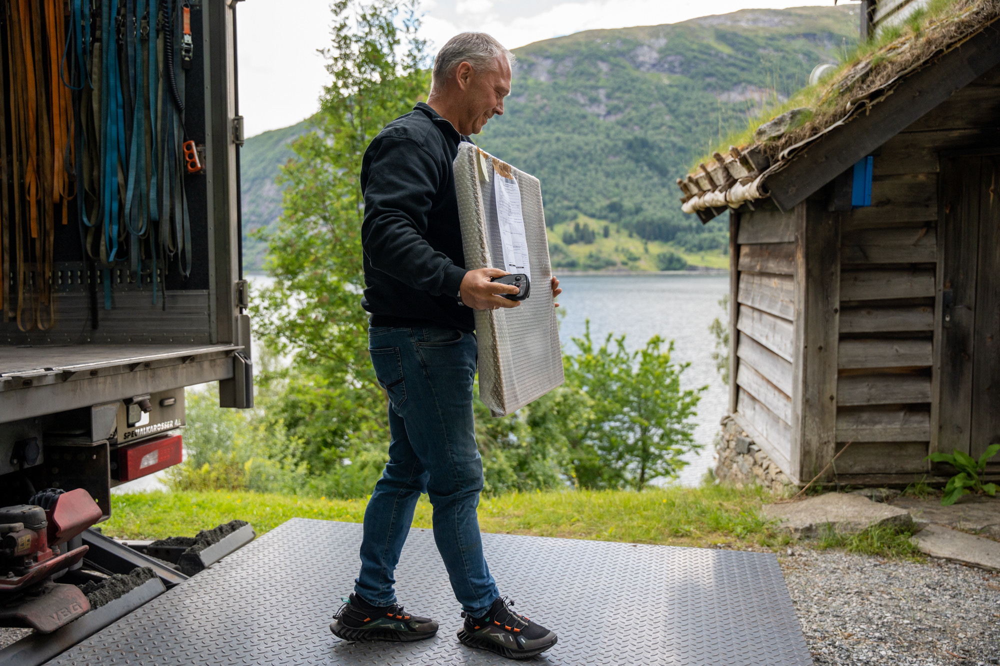 MAnn står på lastelem, held eit måleri innpakka i bobleplast.