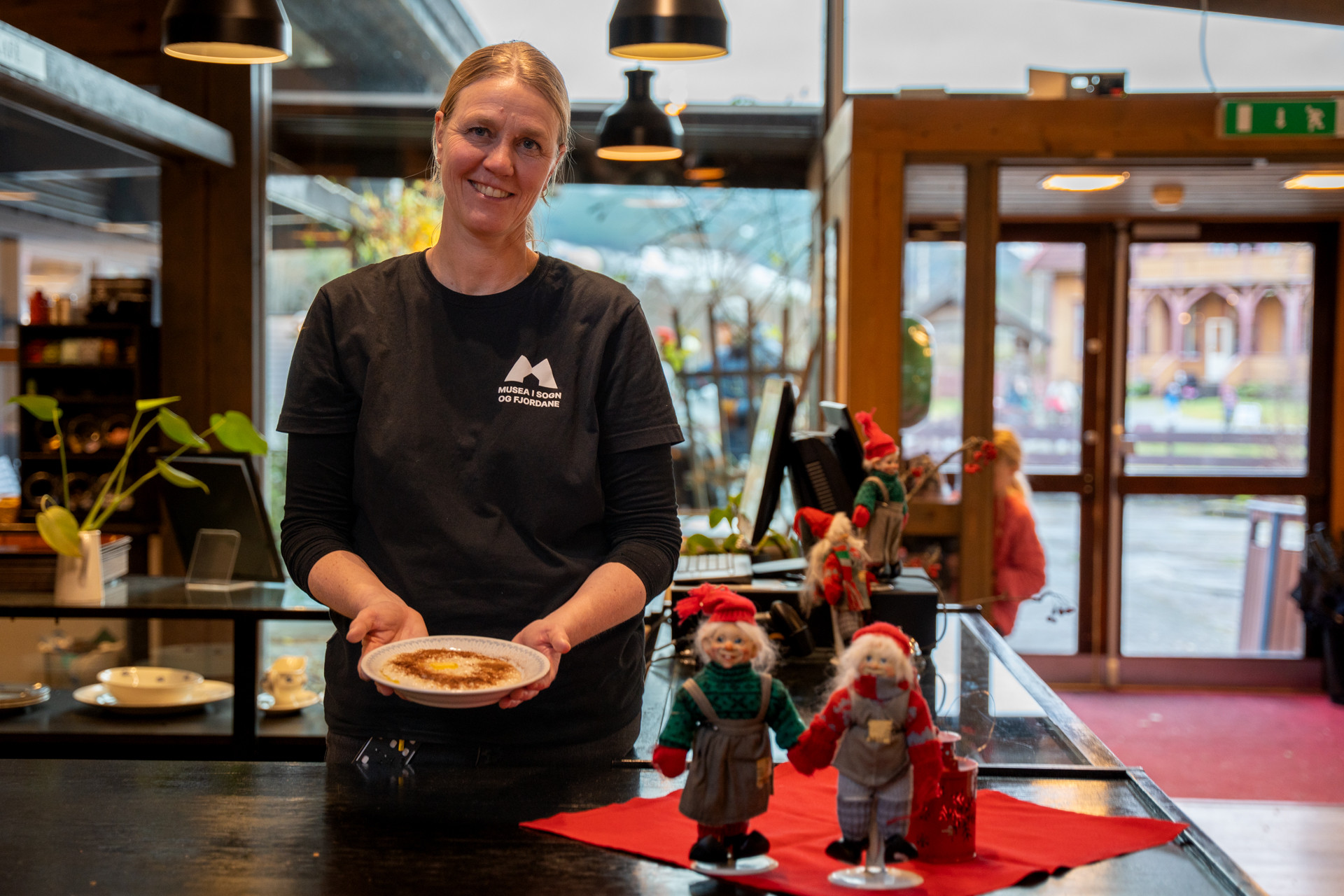 Smilande kvinne held porsjon med risgraut i julepynta kafe.