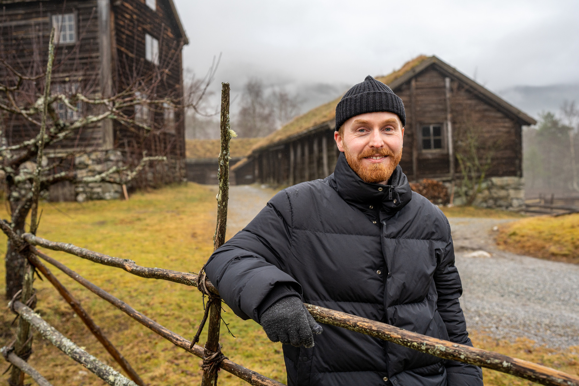 Mann med meskjegg framfor to gamle hus.