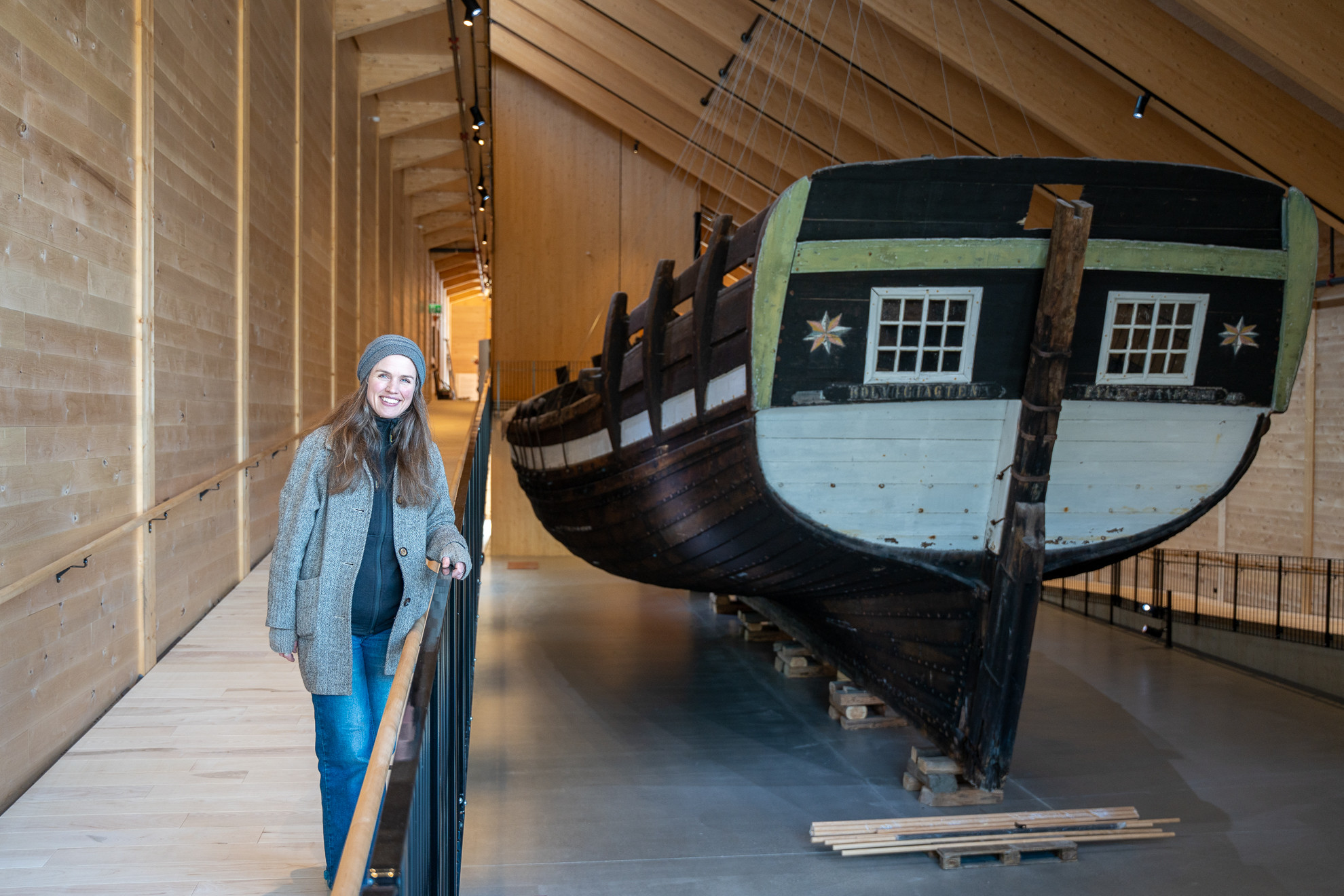 Smilande kvinne står på messanin ved sidan av gamal skute.