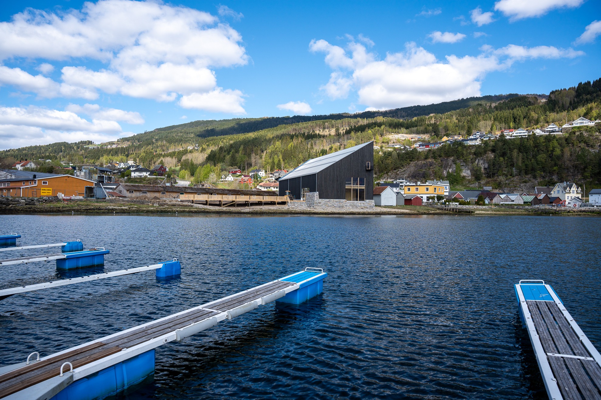 Småbåthavn i forgrunnen, det spisse, svarte bygget til holvikejekta litt på andre sida av fjorden.