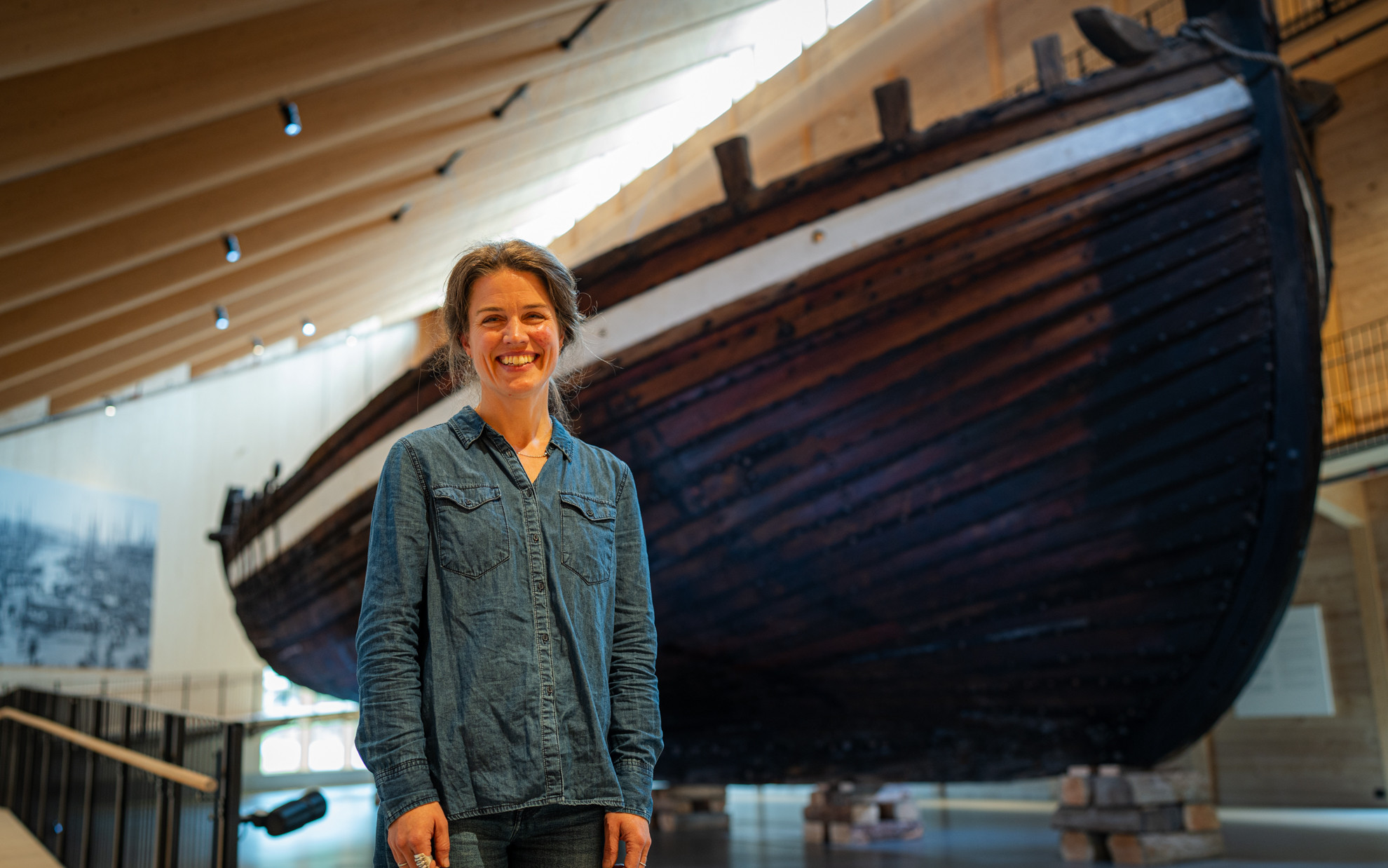 Smilande kvinne framfor stor seglskute inne i museum