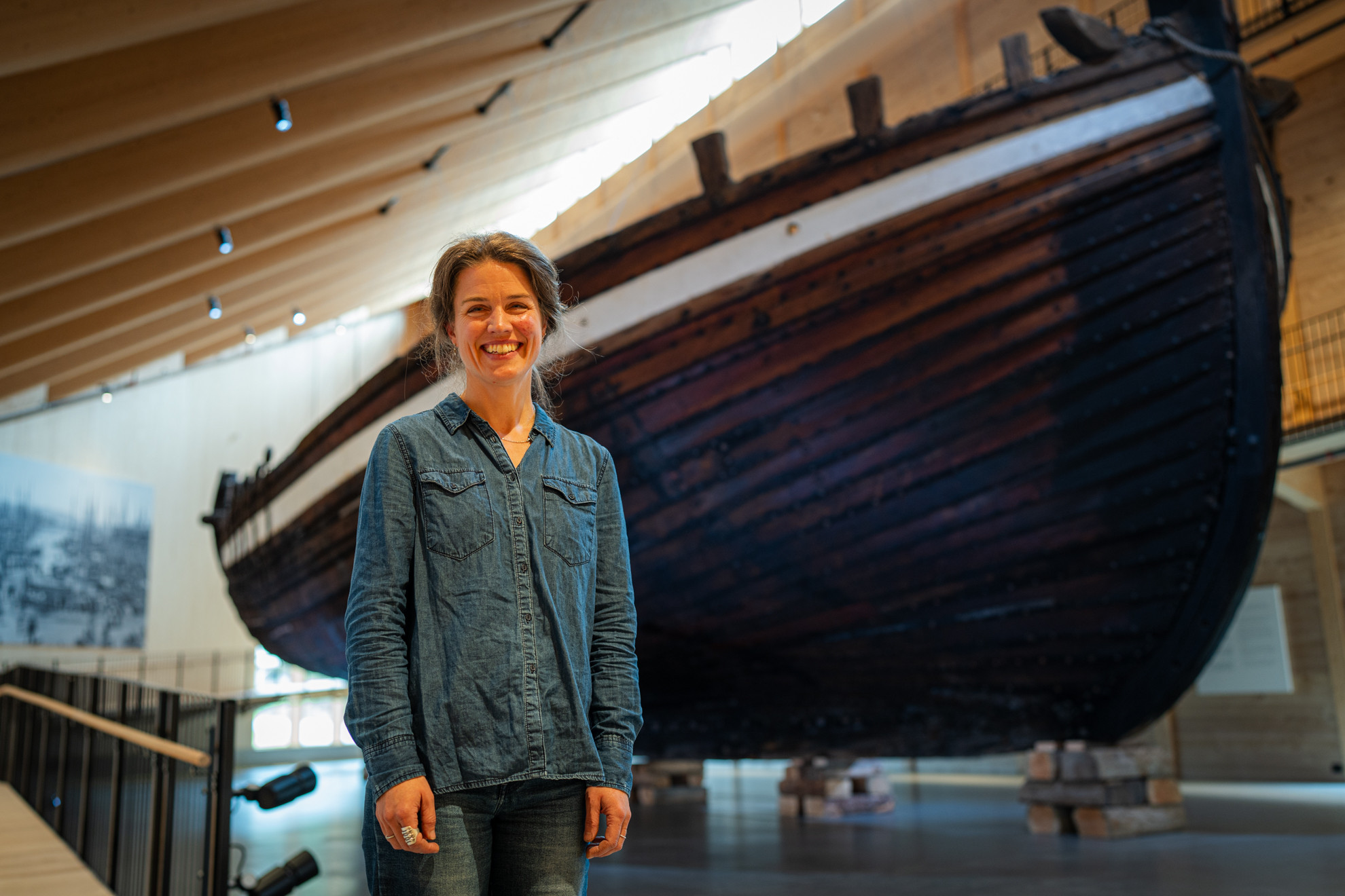 Smilande kvinne framfor stor seglskute inne i museum.