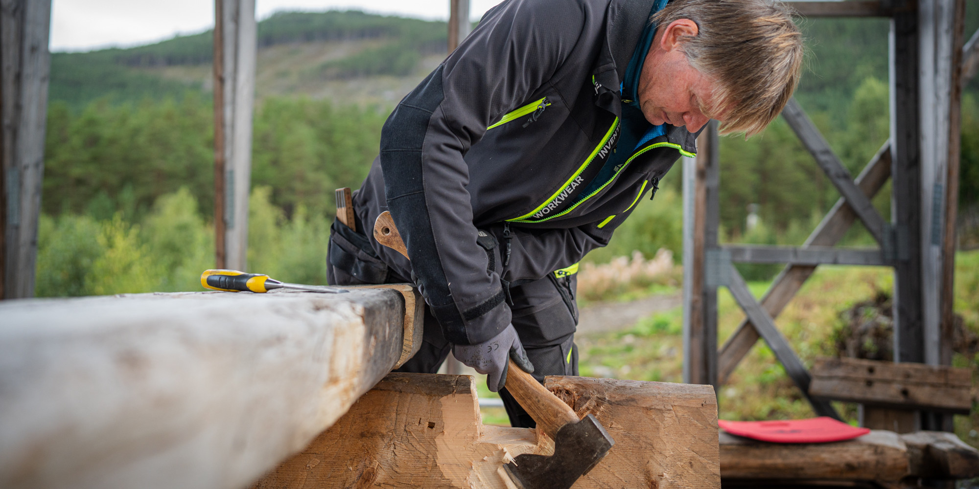 Mann i arbeidsklede høgg med ei øks på ein stokk.
