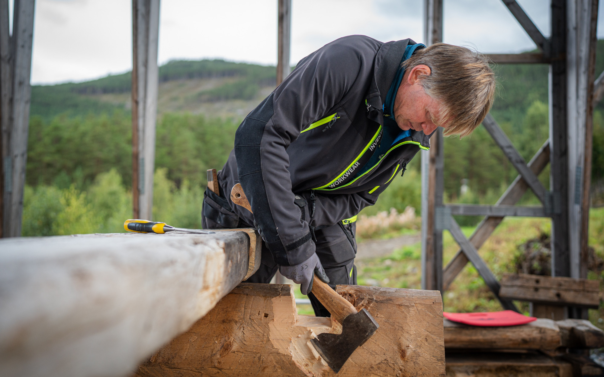 Mann i arbeidsklede høgg med ei øks på ein stokk