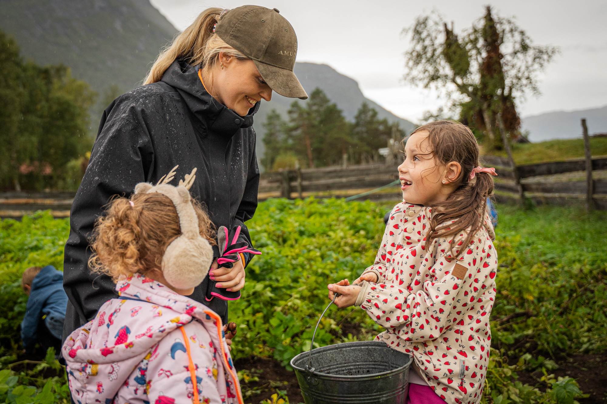 Lita jente held ei bøtte og ser med stort smil på læraren sin.