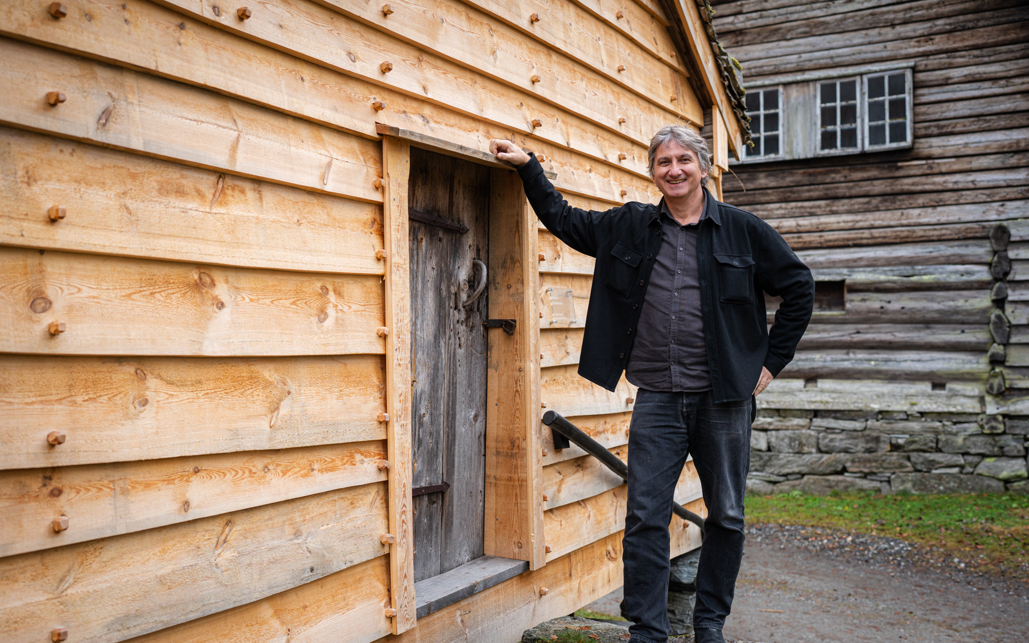 Smilande mann framfor trekvitt stabbur