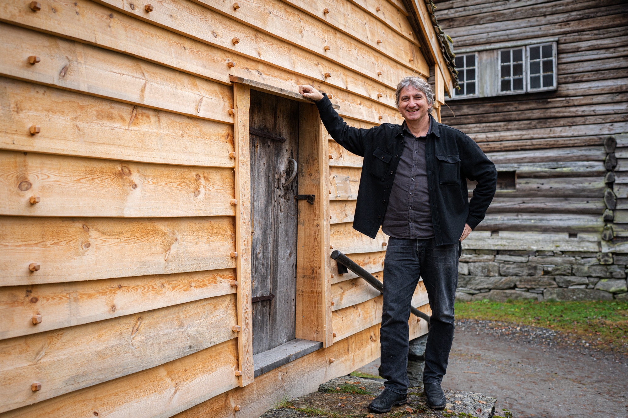 Smilande mann framfor trekvitt stabbur.