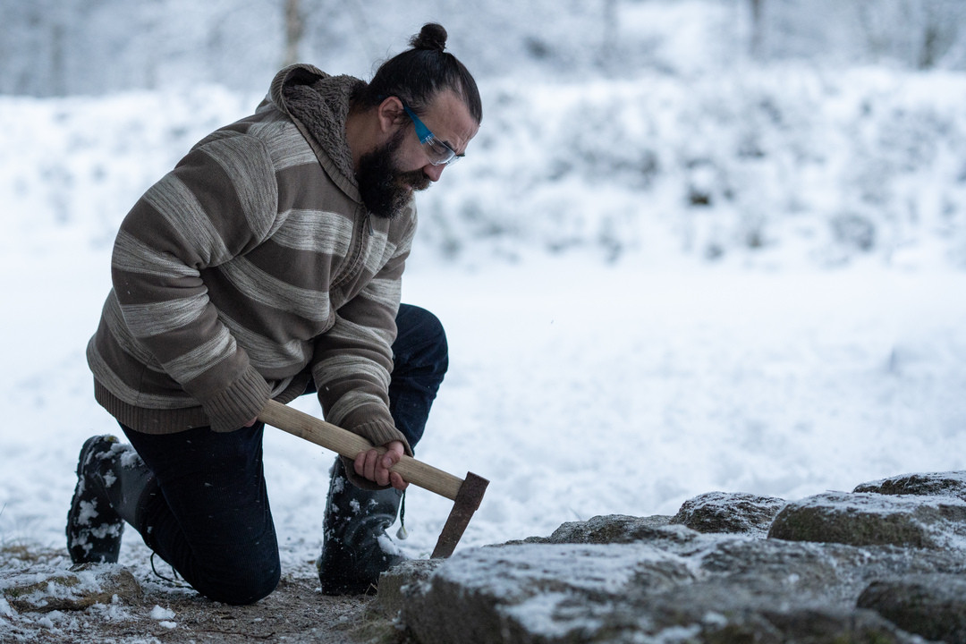 Mann med vernebriller høgg is tein med ei hakke.