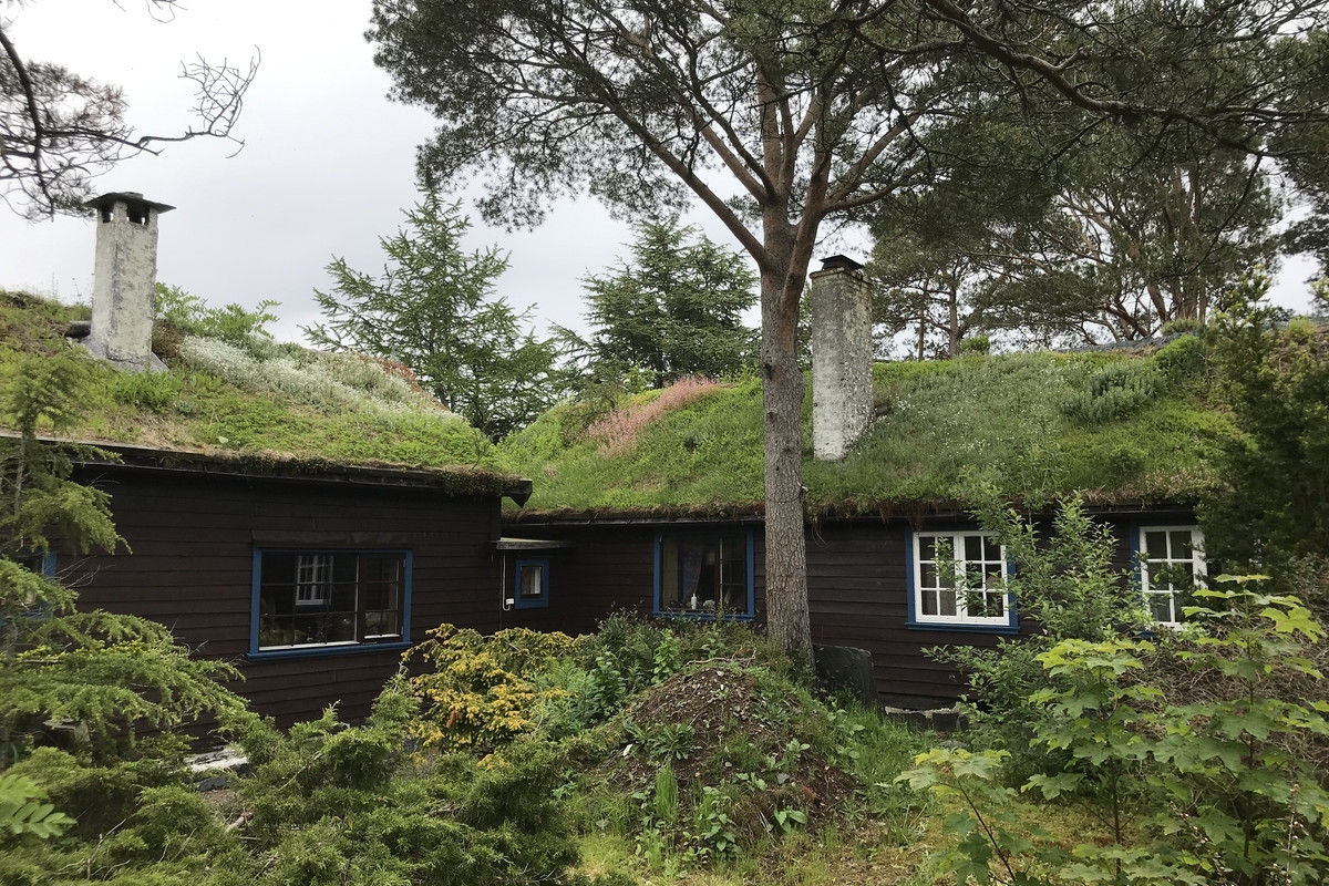 Eit lite brunt hus i ein frodig hage med tre rundt.