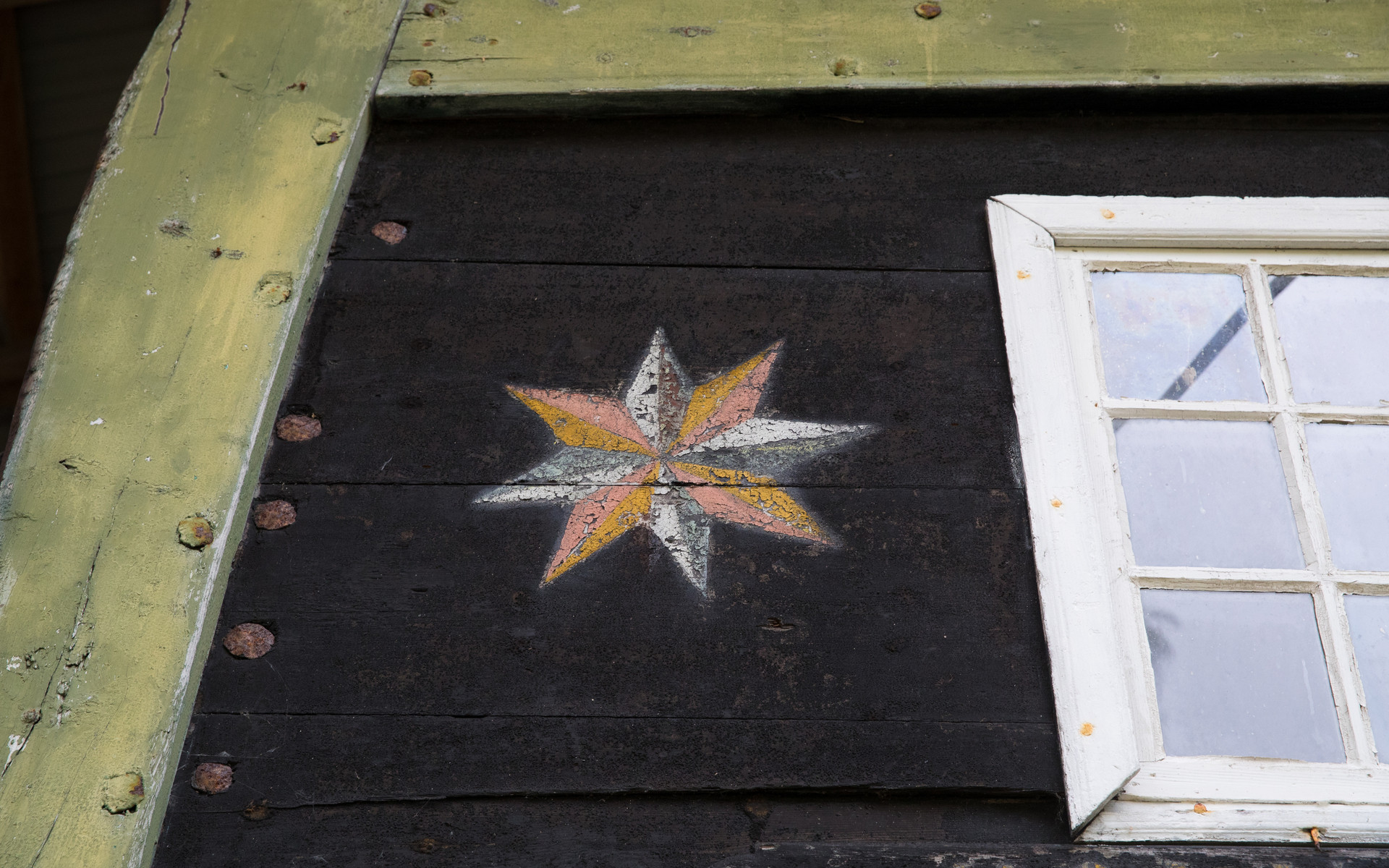 Nærbilde av bakenden på Holvikejekta, ei stjerne i kvitt, gult og fersken ved sidan av eit vindauge.