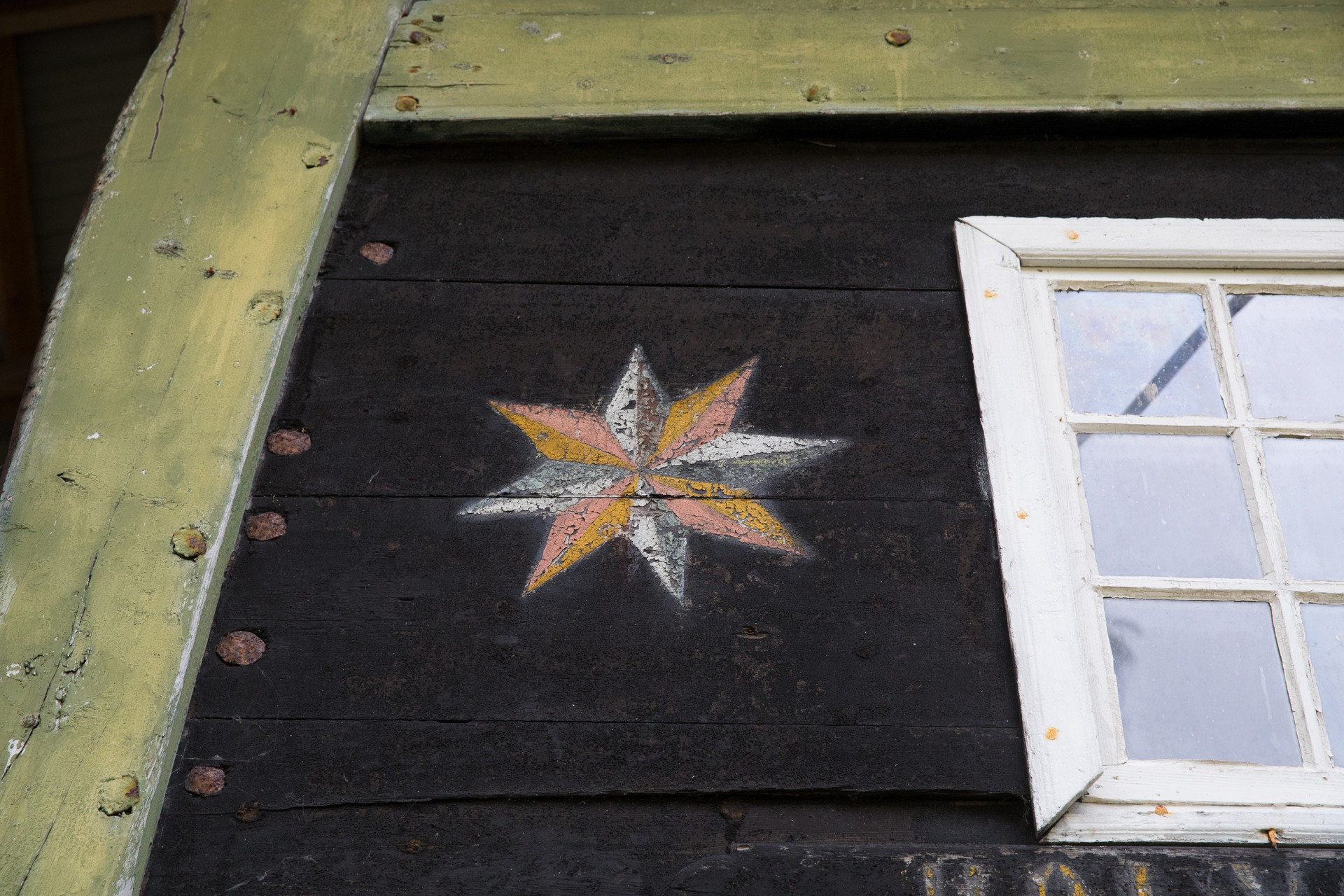 Nærbilde av bakenden på Holvikejekta, ei stjerne i kvitt, gult og fersken ved sidan av eit vindauge.
