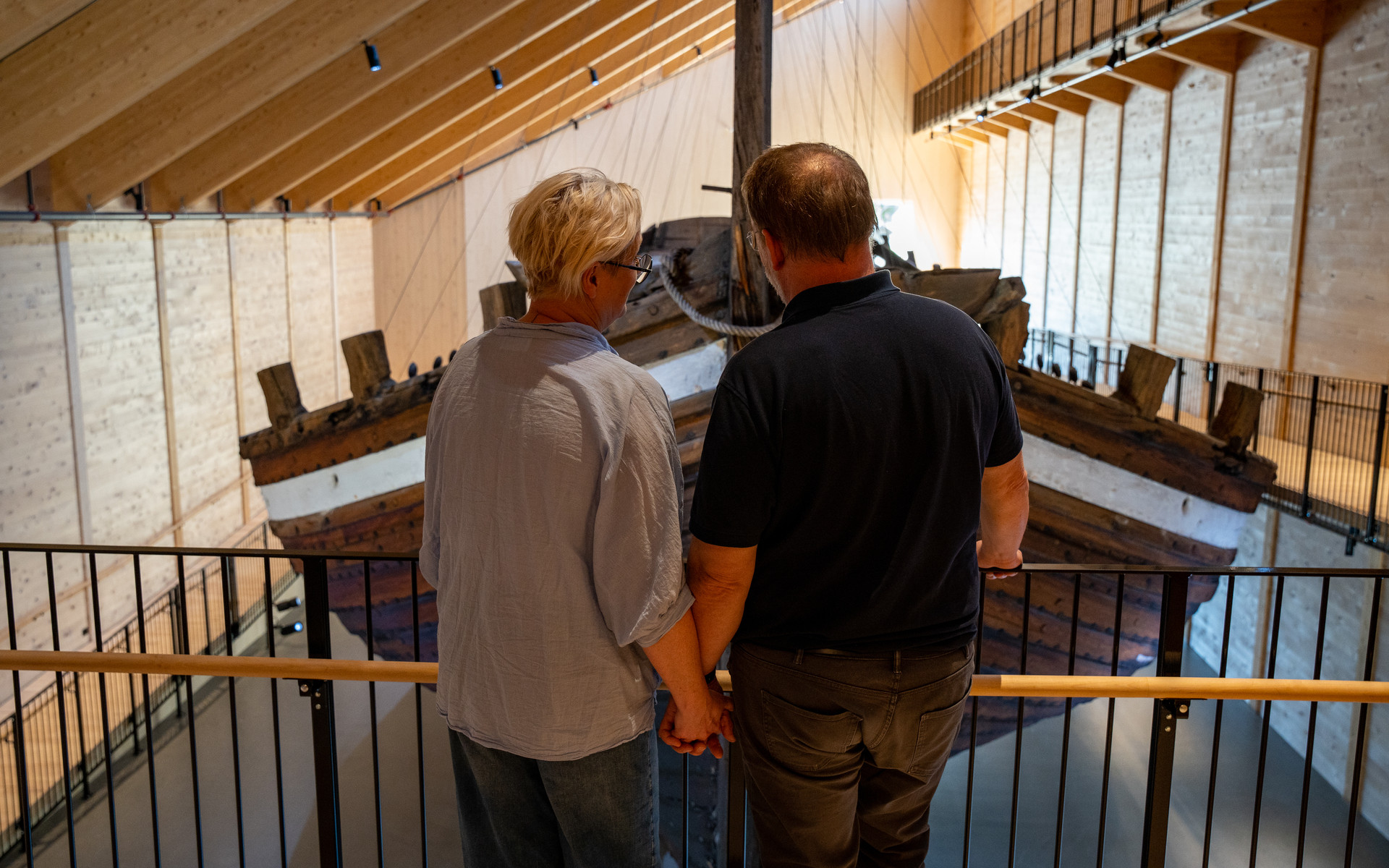 To personar med ryggen til studerer Holvikejekta inne i museet