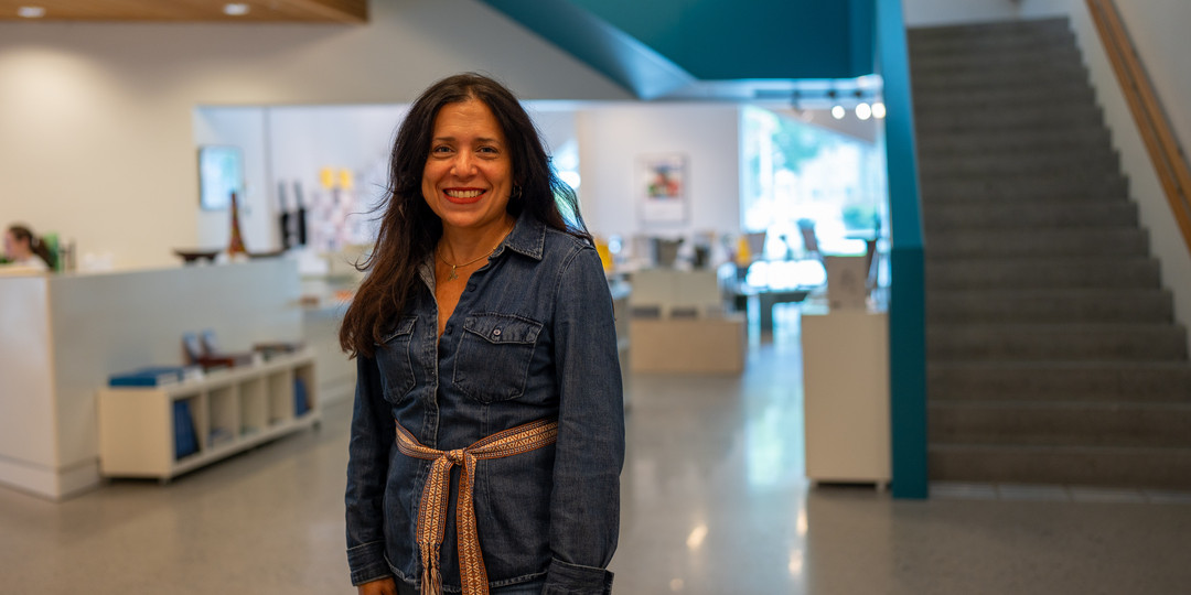 Smilande kvinne med vevd belte står framfor ei turkis trapp i kunstmuseet