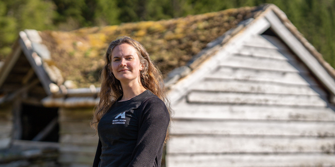 Portrett av kvinne framfor gamal låve