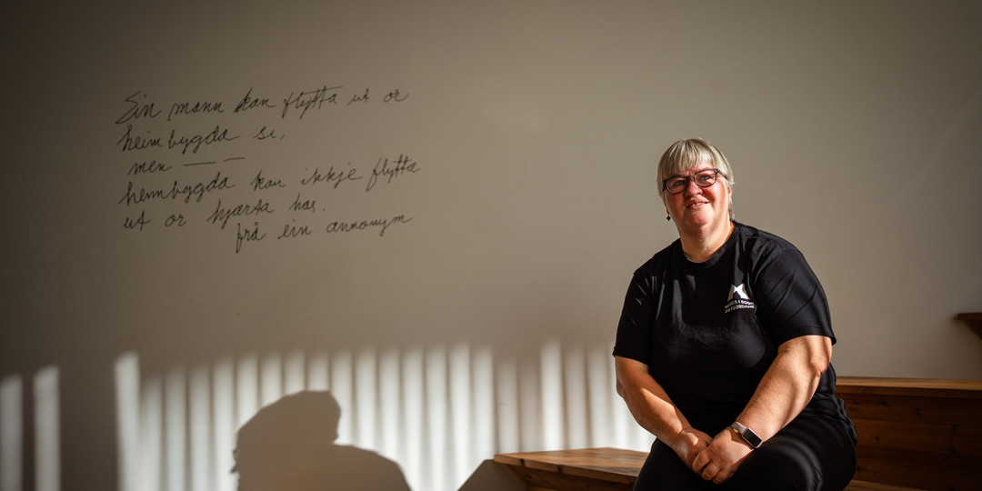 Kvinne sit i ei trapp med sola i ansiktet, skaper skugge på veggen bak