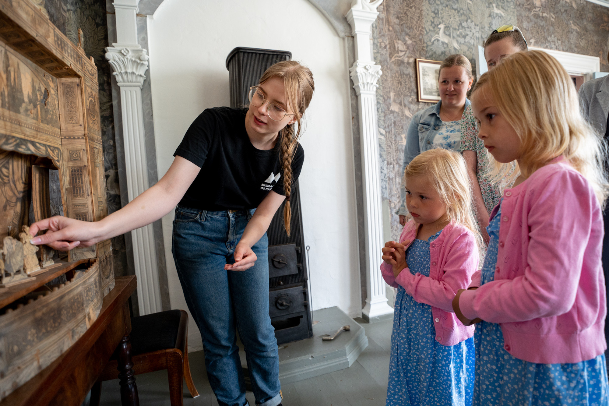 Ein museumsvert viser fram eit historisk dukketeater, to små jenter ser på.
