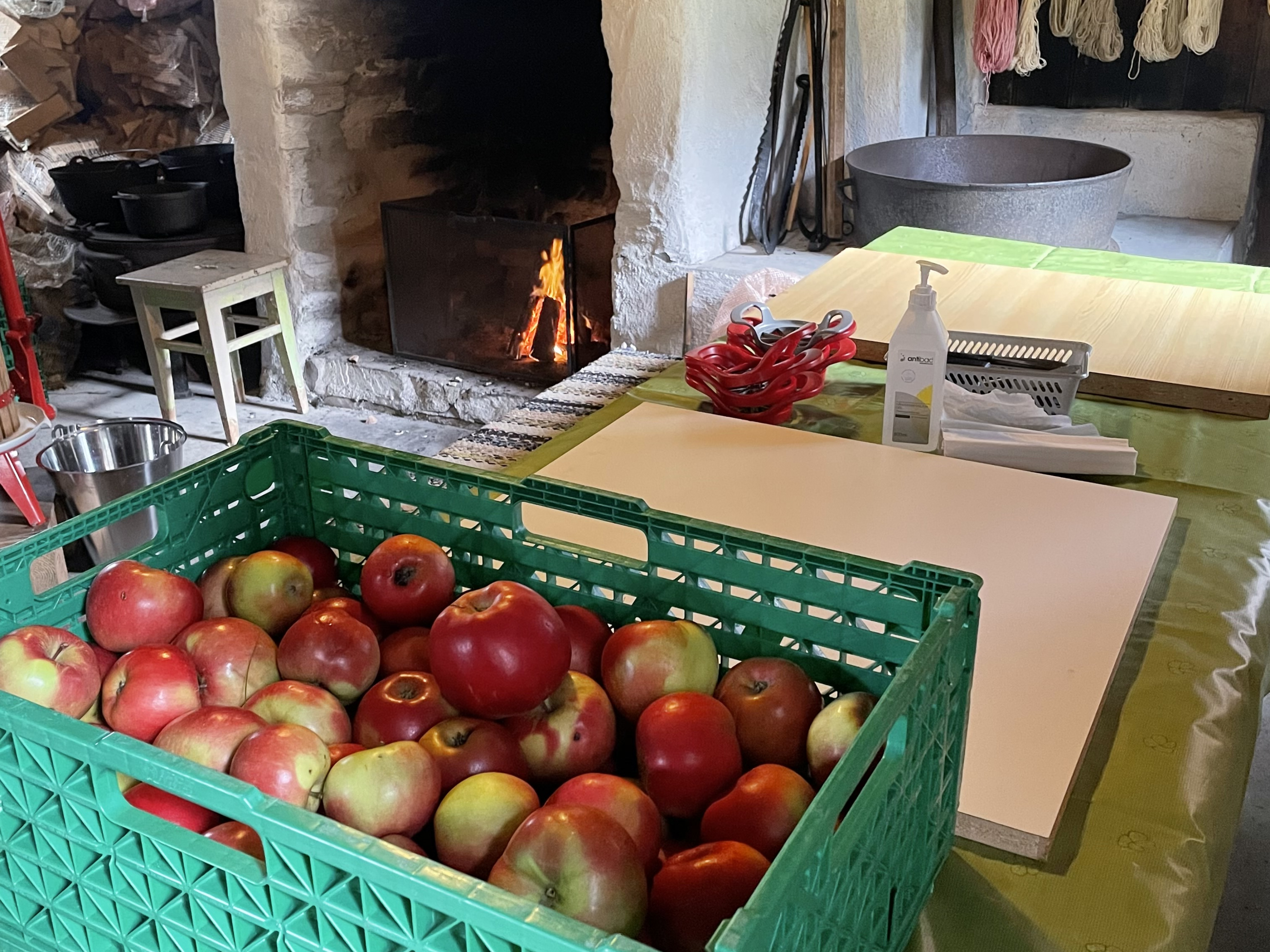 Eit bord med epler og utstyr til eplepressing. Bål i grua.