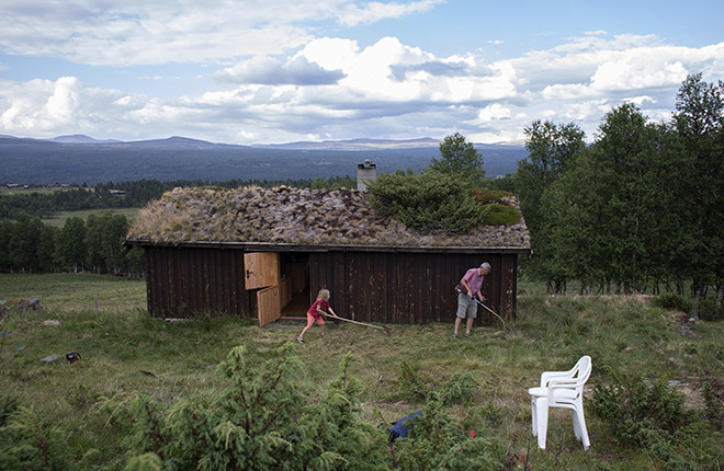 Mann med ryddesag slår graset utanfor ei hytte.