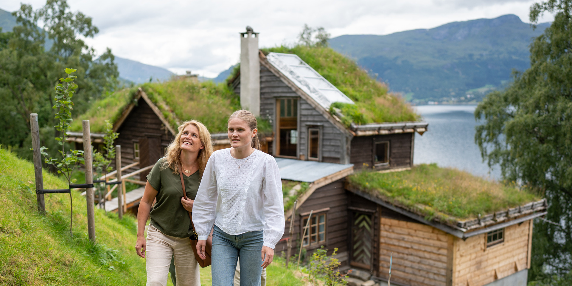 To kvinner går på ein sti med hus med mange vinklar i bakgrunnen.