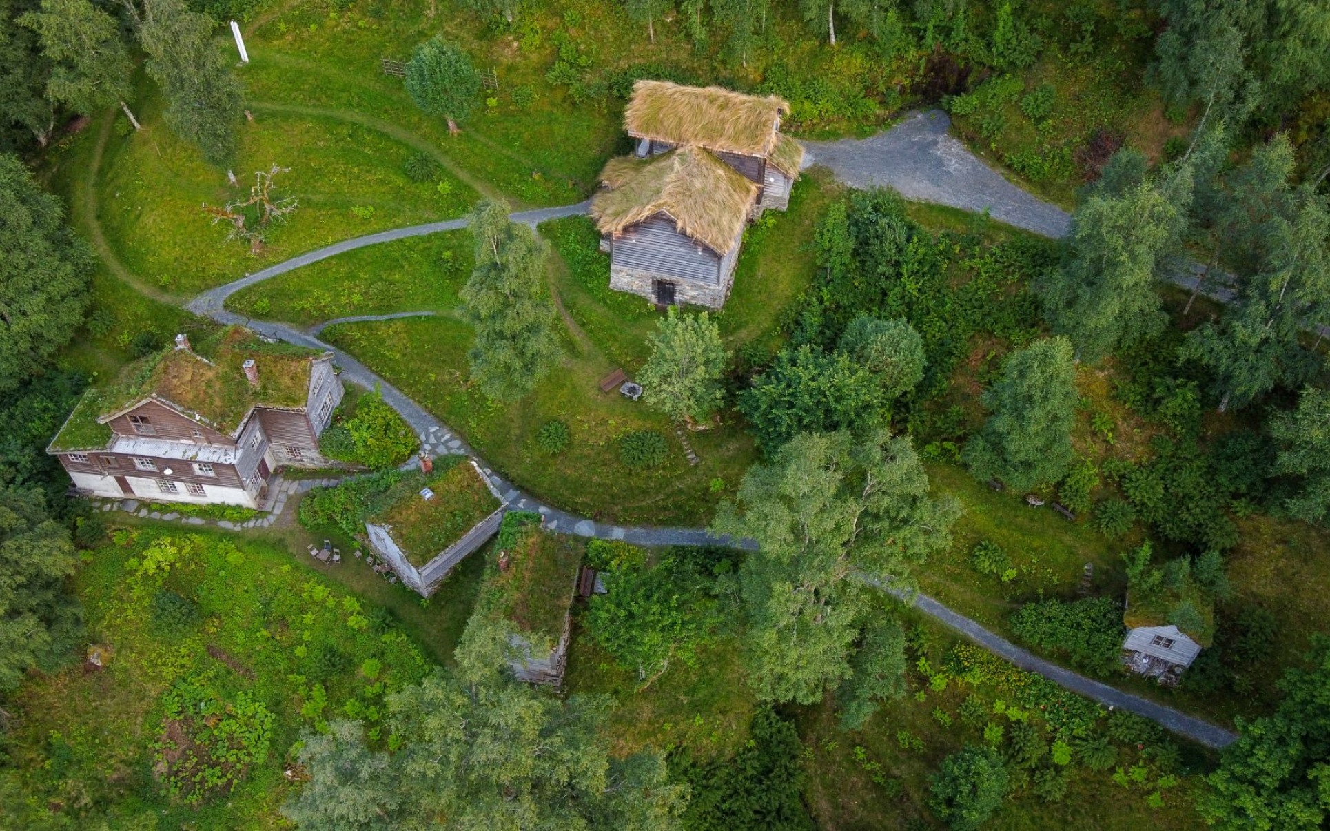 Flyfoto av kunstnharheimen til Nikolai Astrup, Astruptunet, der vi ser smale grusvegar bukte seg mellom grå bygningar med torvtak. Her kan du få omvisning.