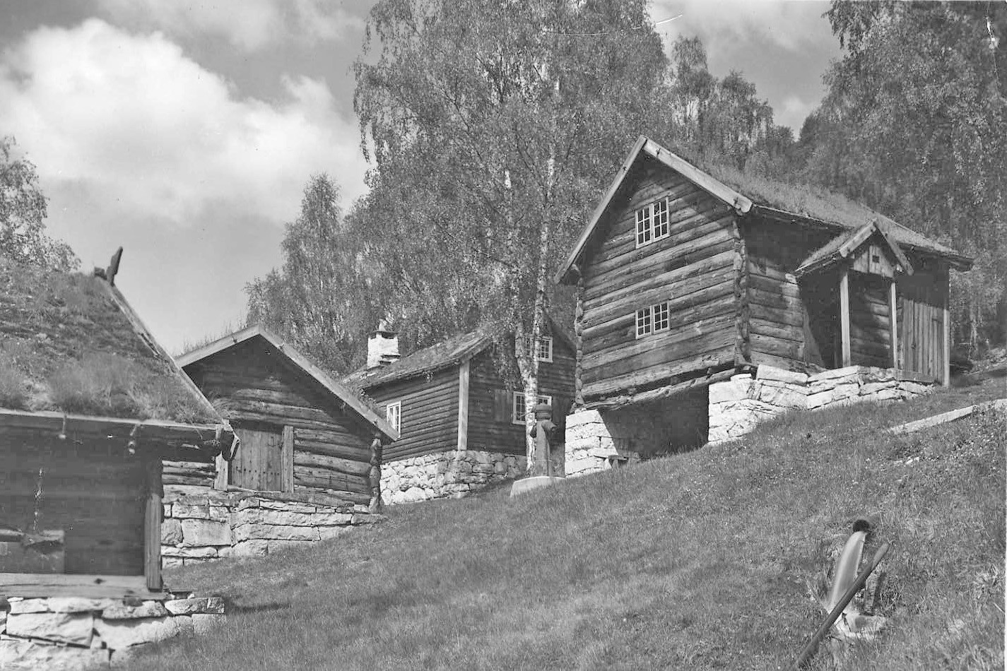 Svart-kvitt bilde av fleire gamle hus som står på kvite murar i ein skrå bakke.