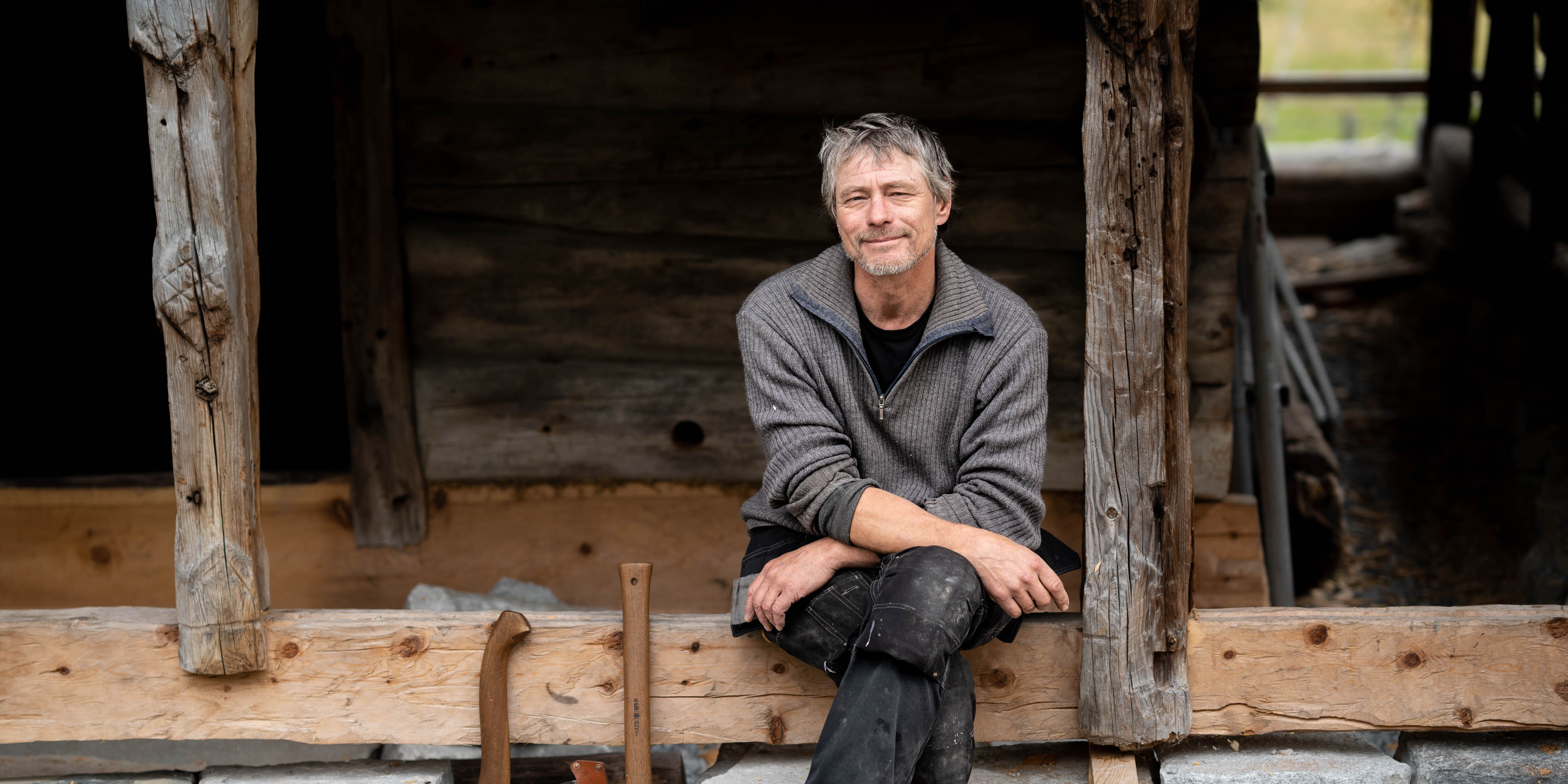 Kjetil Bergmo sit på ein stokk i ein opning med øksene ved sidan av seg.