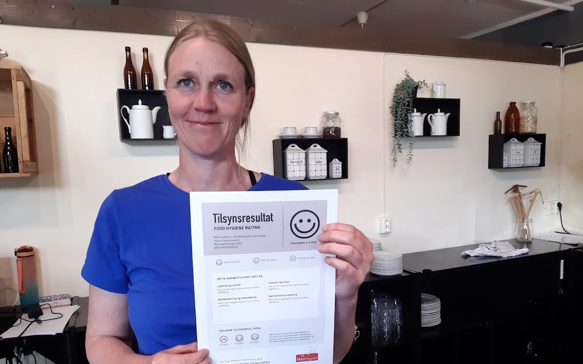Kvinne i blå t-skjorte held opp eit dokument frå mattilsynet med smilefjes