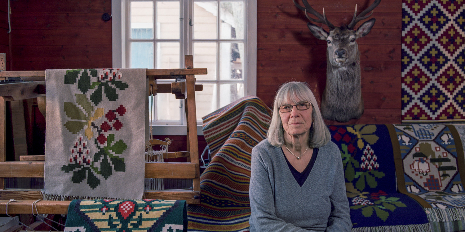 Kvinne midt i eit rom med tekstilar rundt seg.