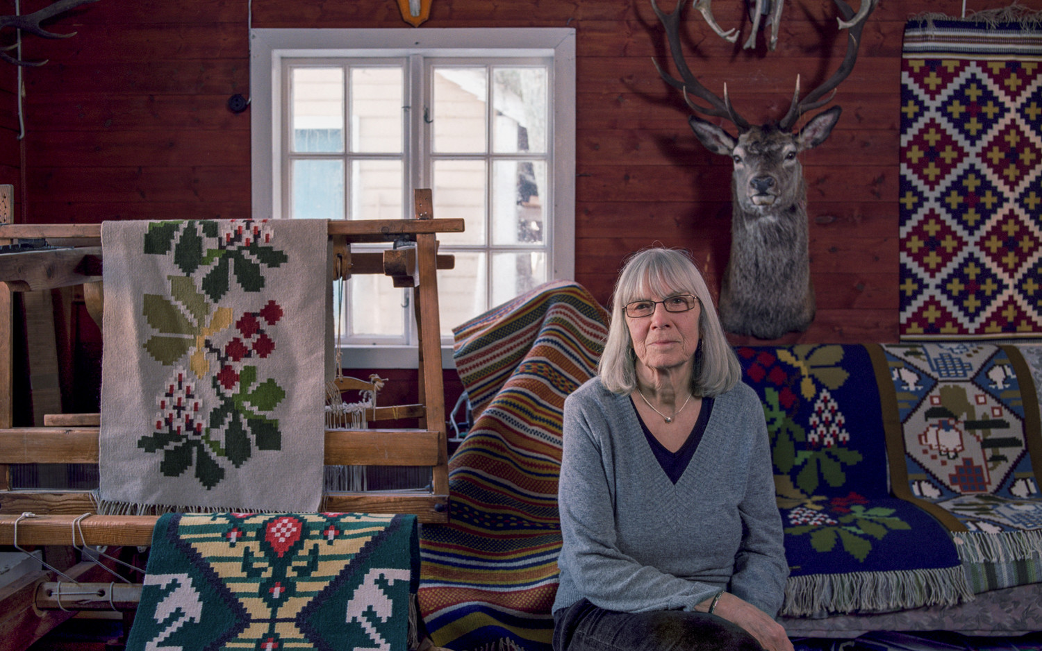 Kvinne midt i eit rom med tekstilar rundt seg